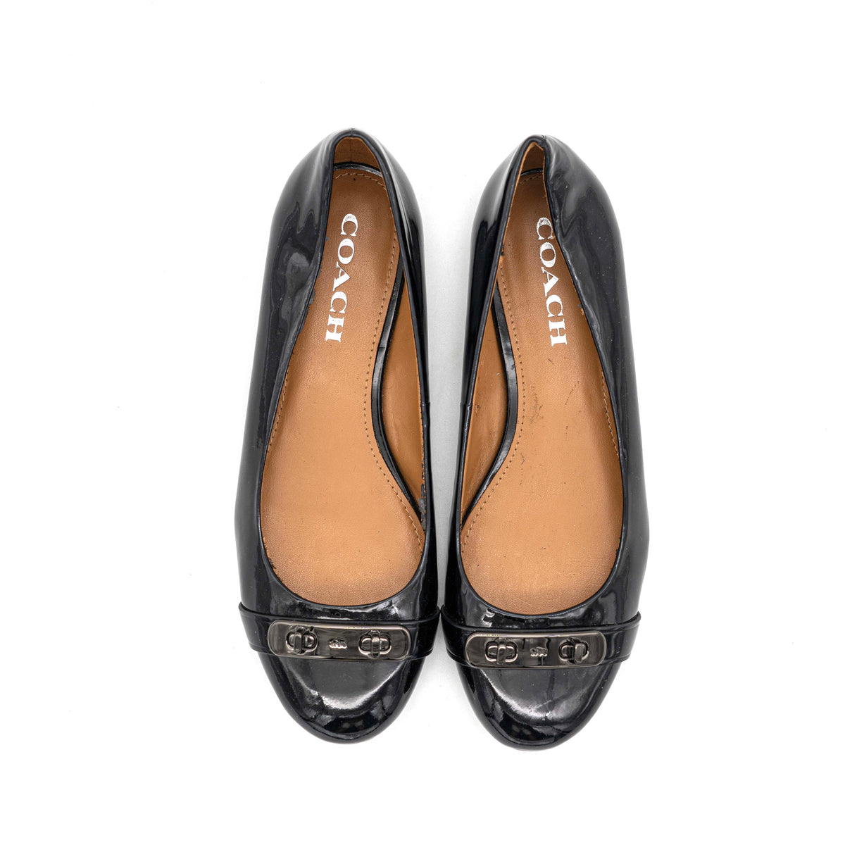Coach Oswald Turnlock black patent leather ballet flats with dark metal hardware on the toe, photographed on a white background.