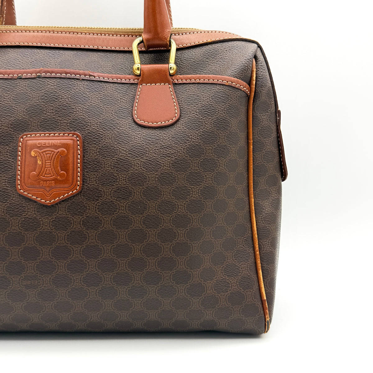 Celine Triomphe Macadam Boston Bag in brown coated canvas with tan leather handles and gold hardware on a white background.