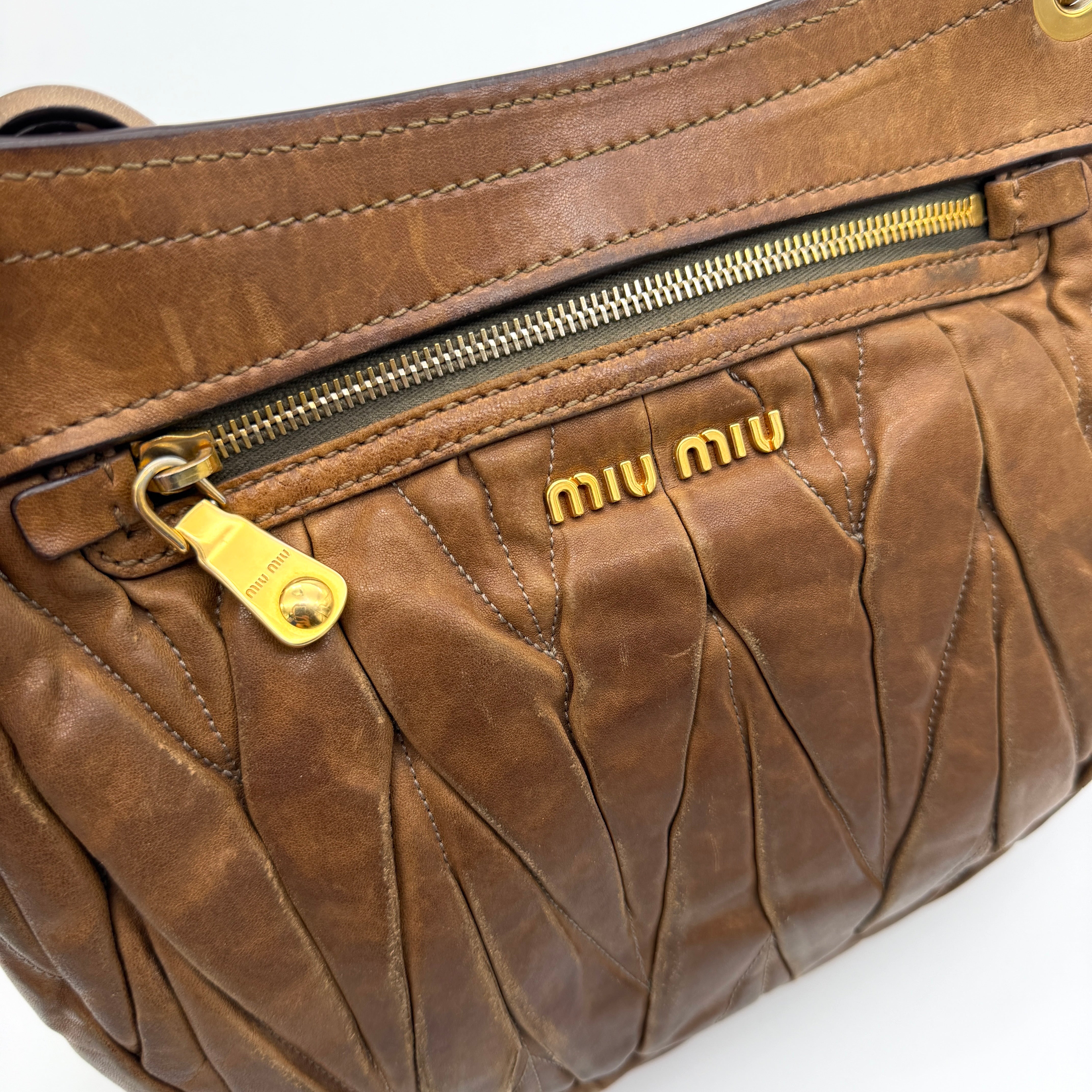 Miu Miu brown Matelasse Coffer Hobo bag with gold hardware, detachable strap, and dust bag displayed on a flat surface.