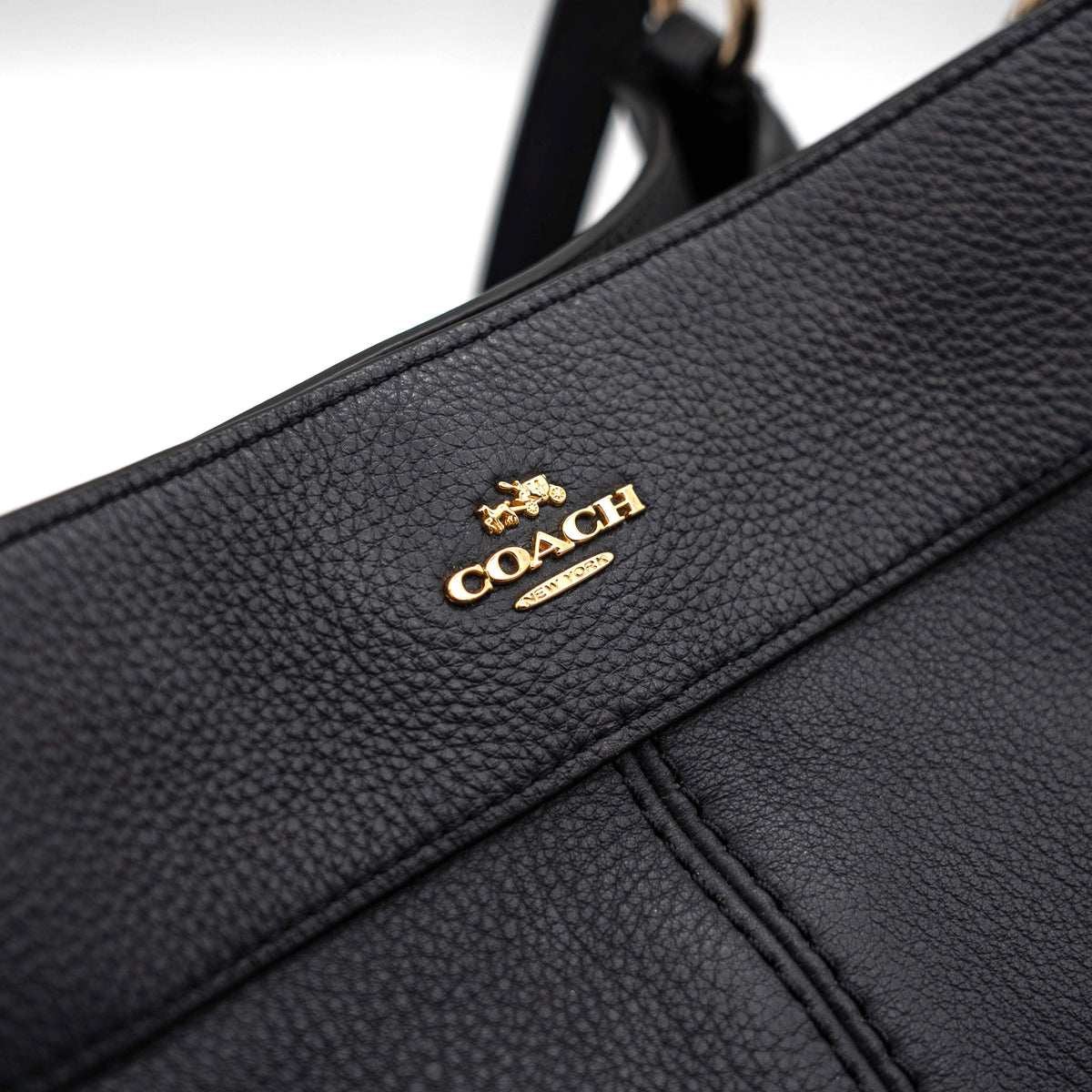 Coach Lexy Shoulder Bag in black pebbled leather with gold-tone hardware and double handles, styled against a white background.