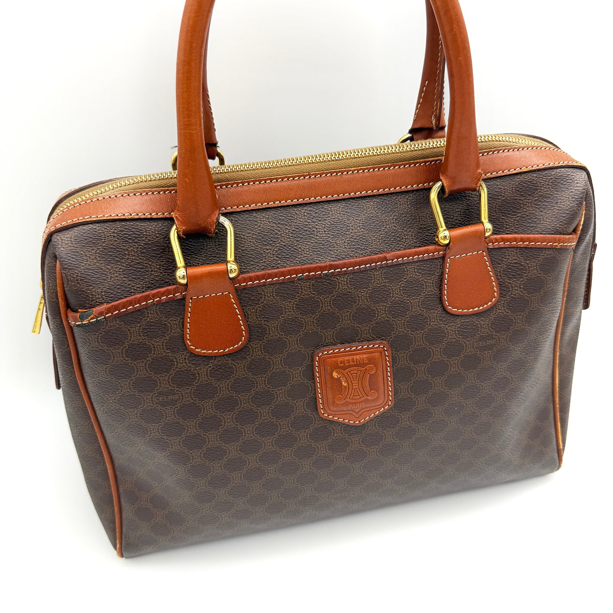 Celine Triomphe Macadam Boston Bag in brown coated canvas with tan leather handles and gold hardware on a white background.
