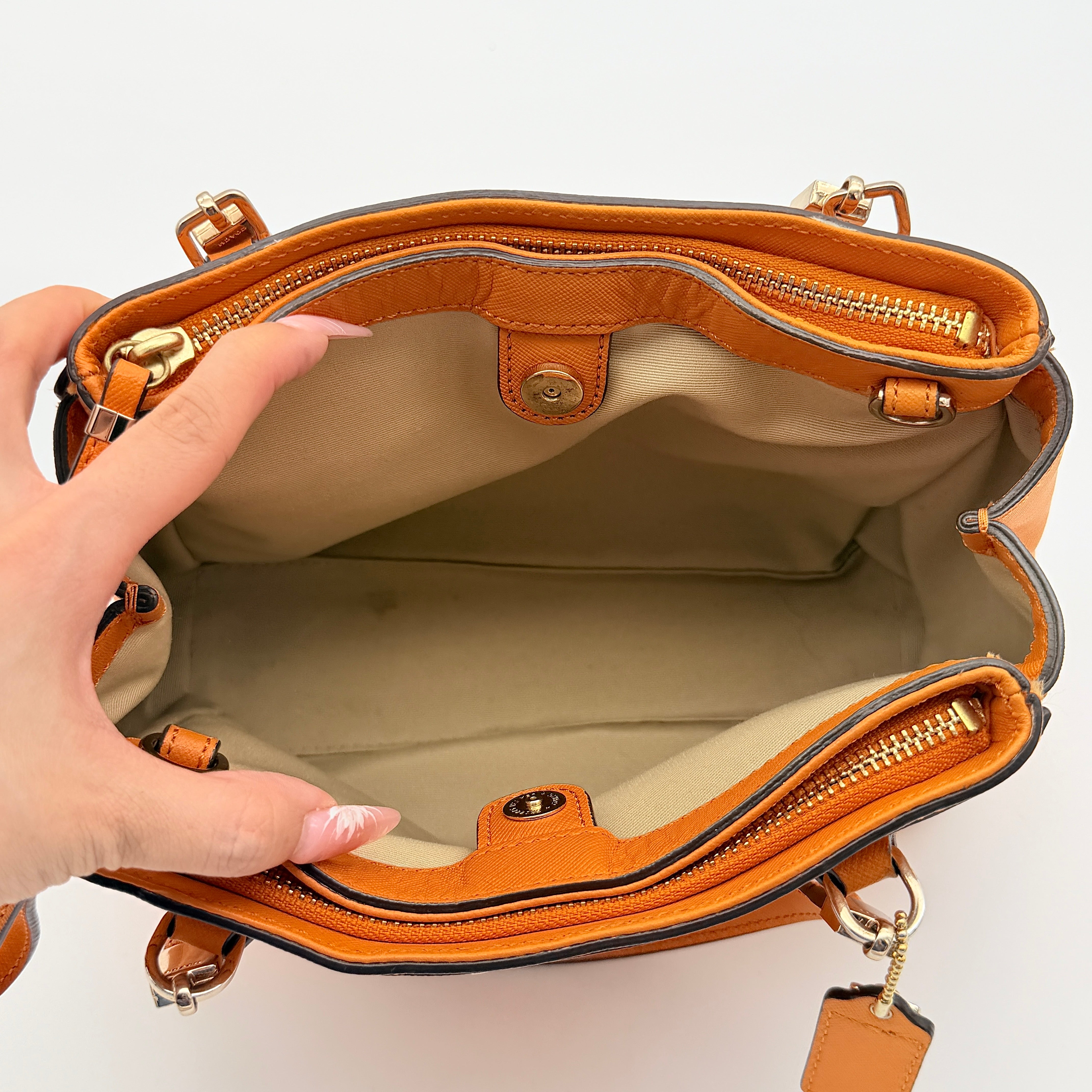 Coach Christie Carryall handbag in orange leather with gold hardware and structured handles, photographed on a white background.