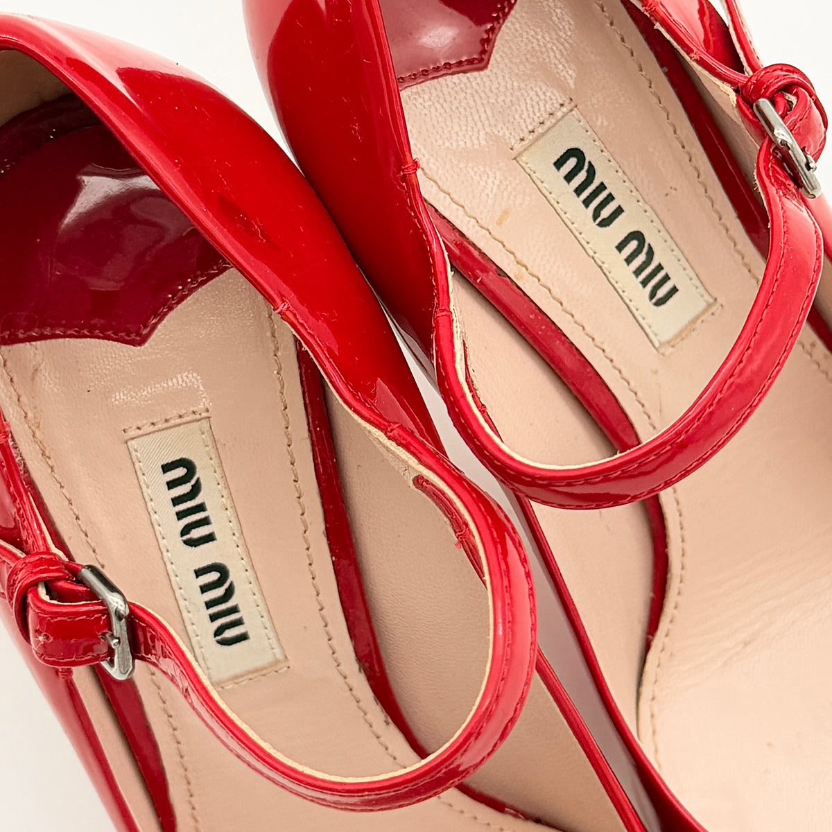 A pair of red patent leather Miu Miu Mary Jane heels with adjustable buckle straps and high heels, displayed against a white background.