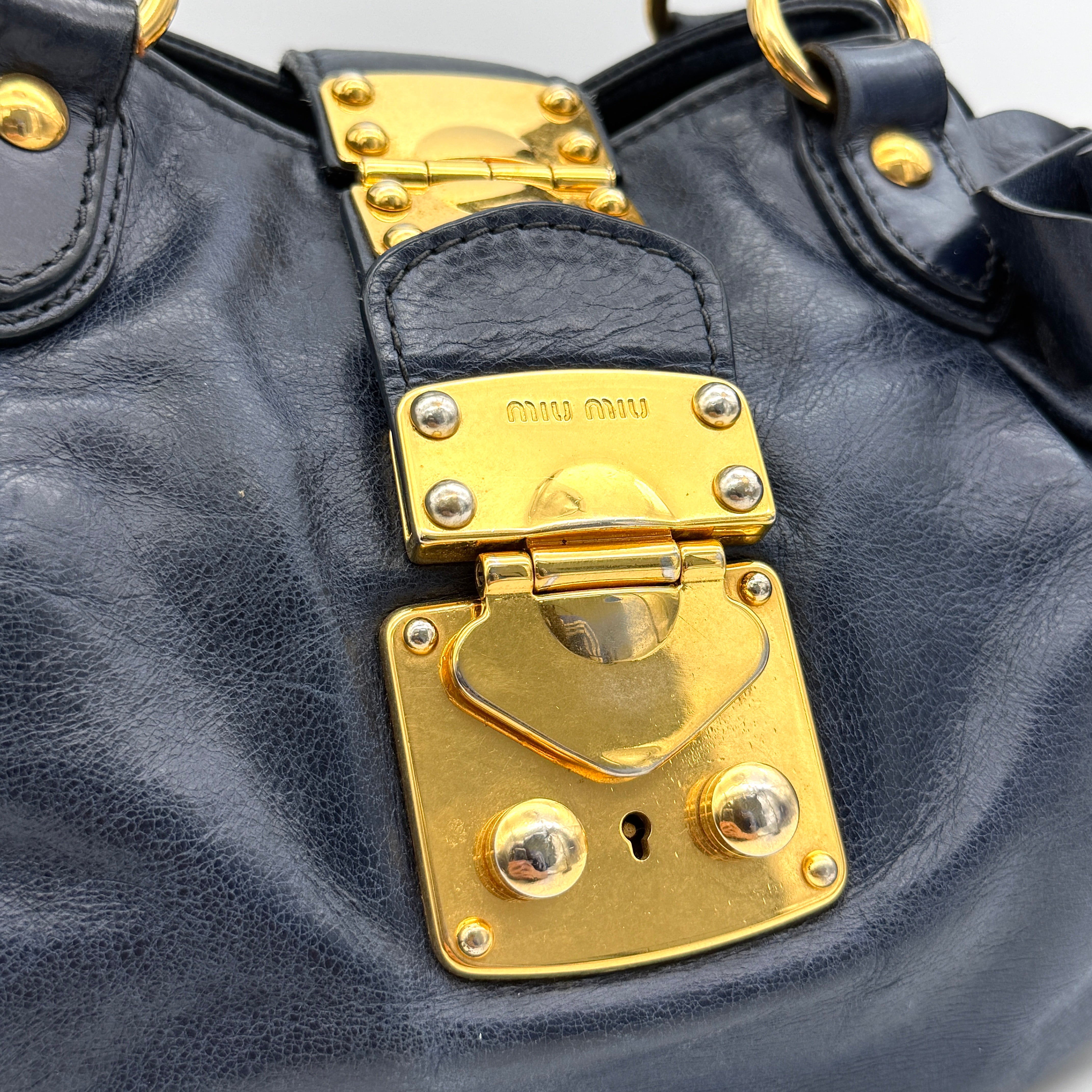Miu Miu navy blue Vitello Lux Bow Satchel with gold-tone hardware, detachable strap, and dust bag.