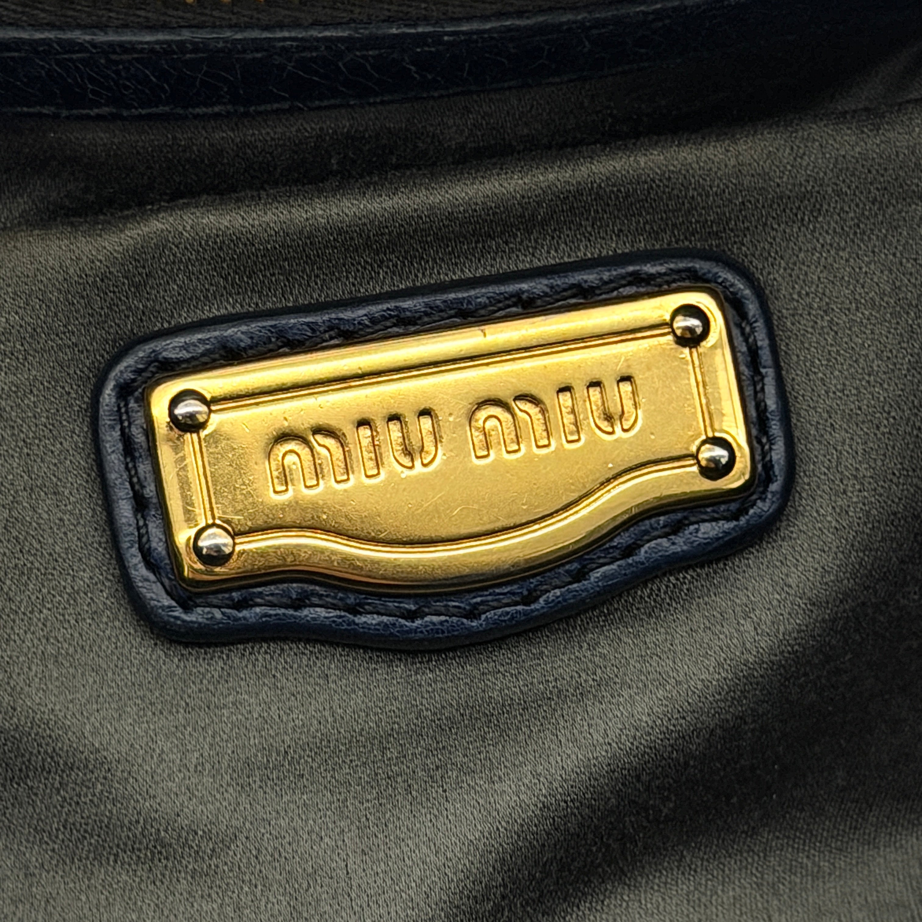 Miu Miu navy blue Vitello Lux Bow Satchel with gold-tone hardware, detachable strap, and dust bag.