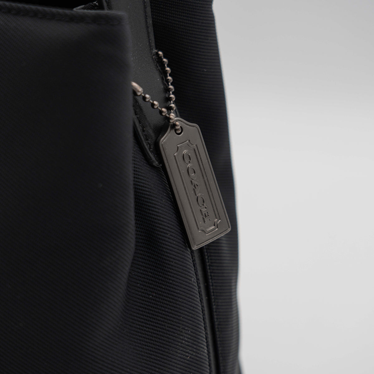Coach Mercer tote bag in black nylon with leather handle and trim, presented against a white background.