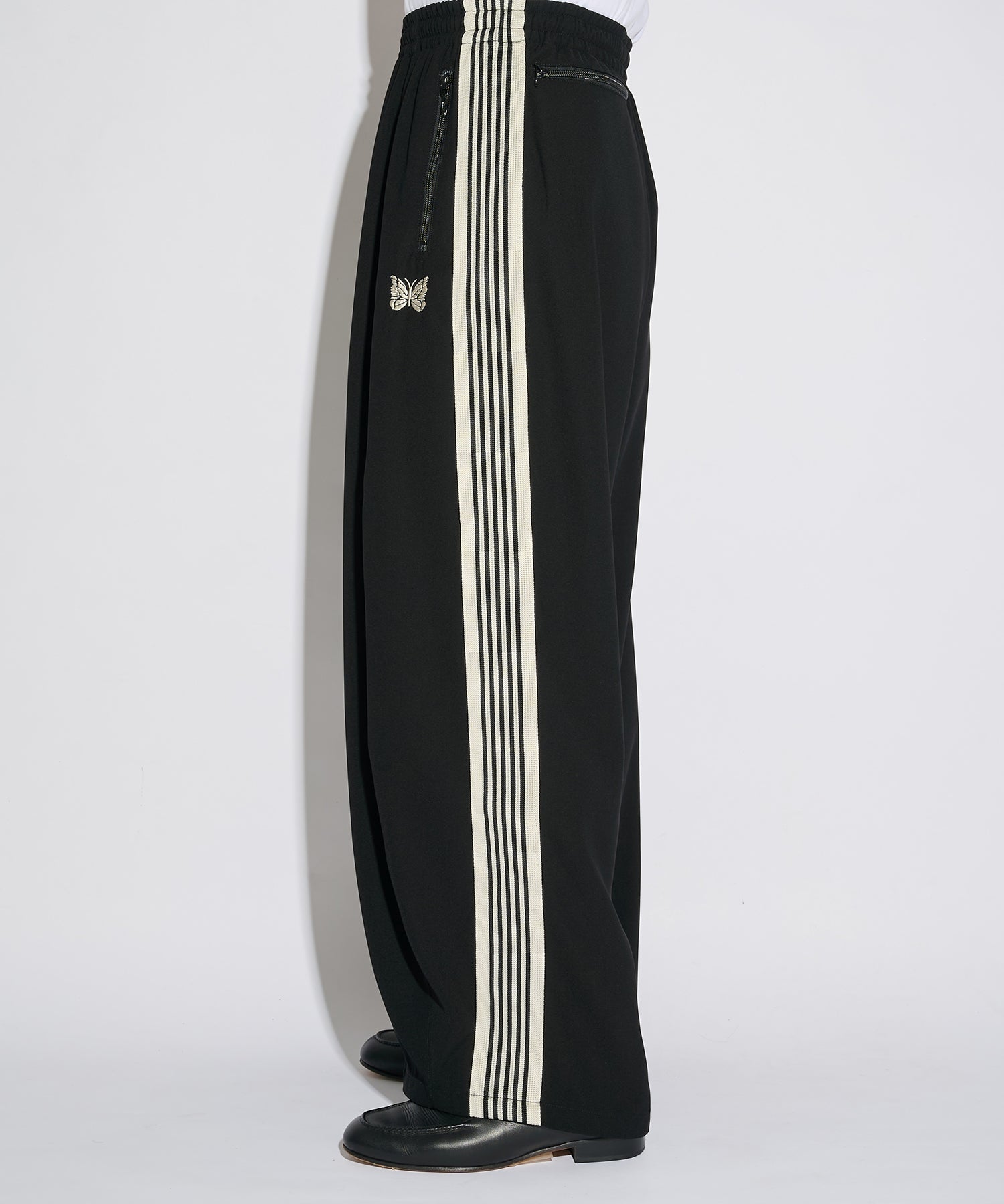 Needles H.D. Track Pant in black with white stripes and butterfly logo, shown in a full-length styled view.