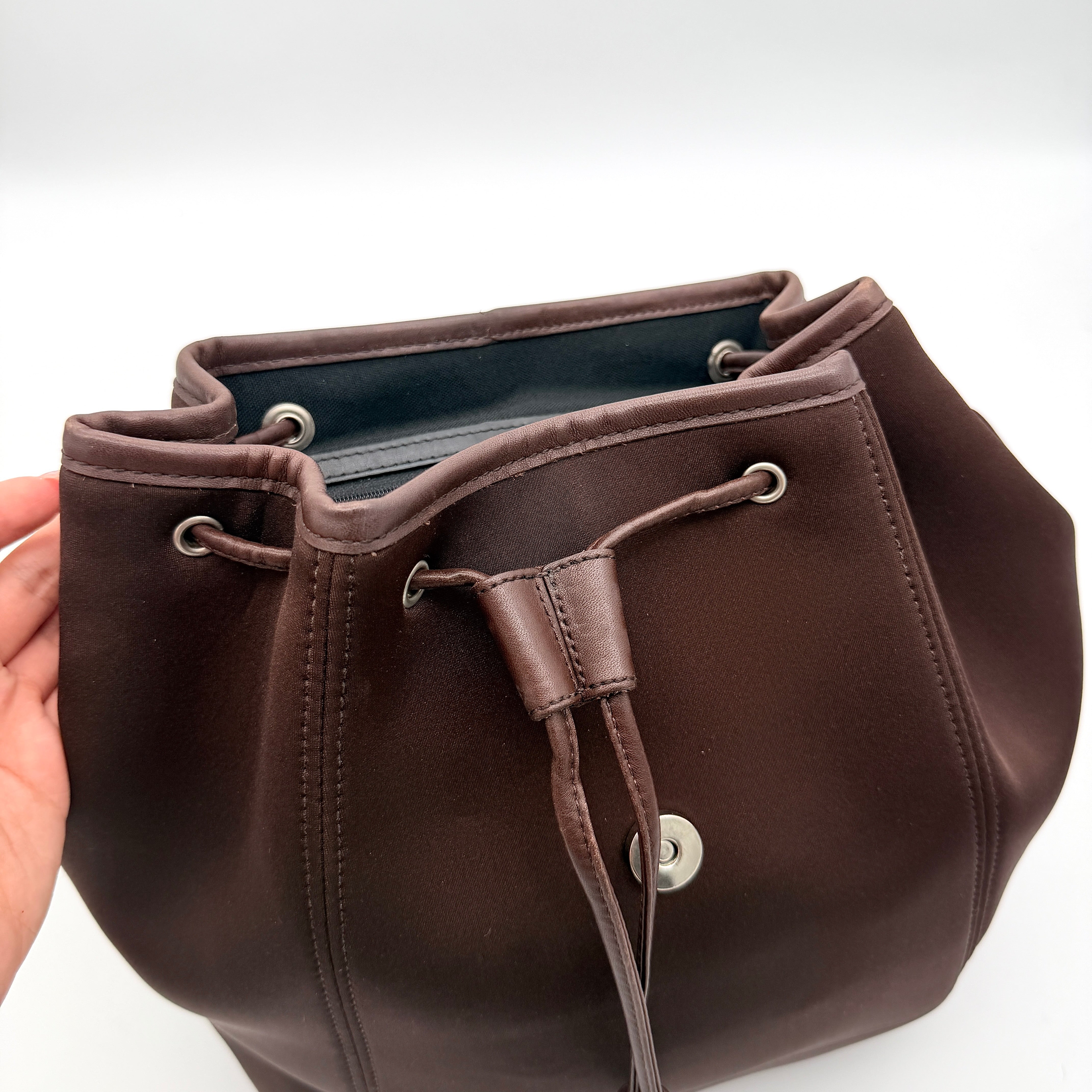Coach brown neoprene drawstring backpack with leather trim, silver-tone hardware, and adjustable straps shown against a white background.