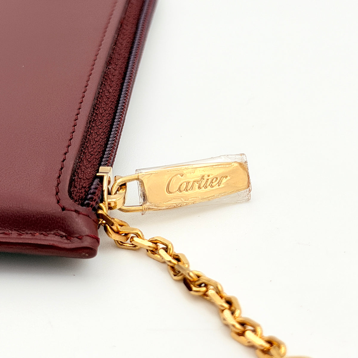 Cartier Must de Cartier burgundy leather coin purse with gold chain key holder and embossed logo, photographed on white.