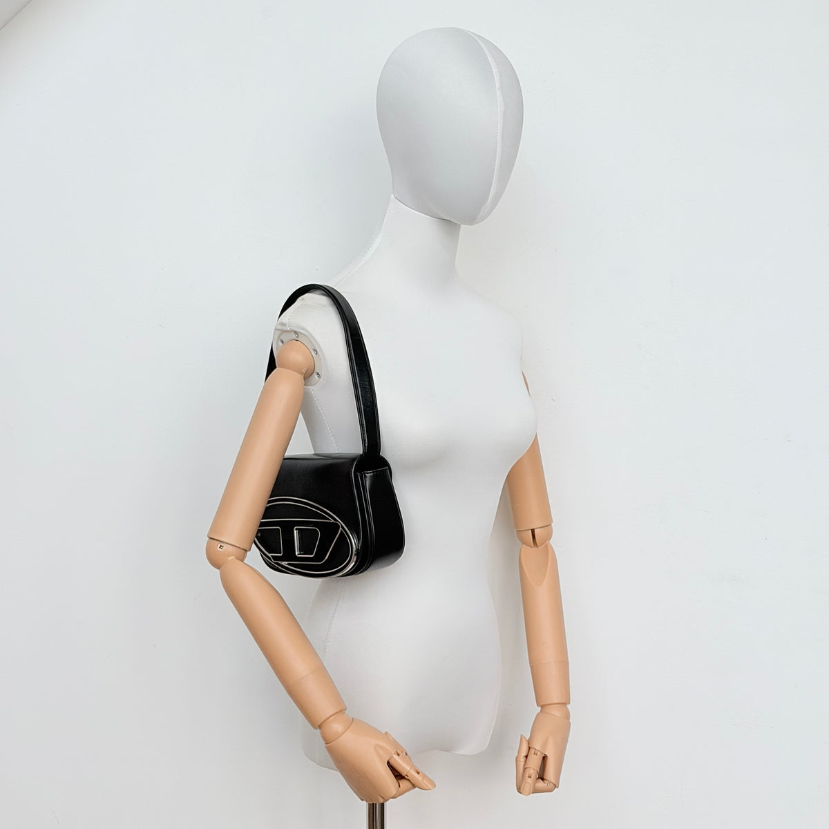 Diesel 1DR Shoulder Bag in black leather with a bold silver and black D logo plaque on the front flap.