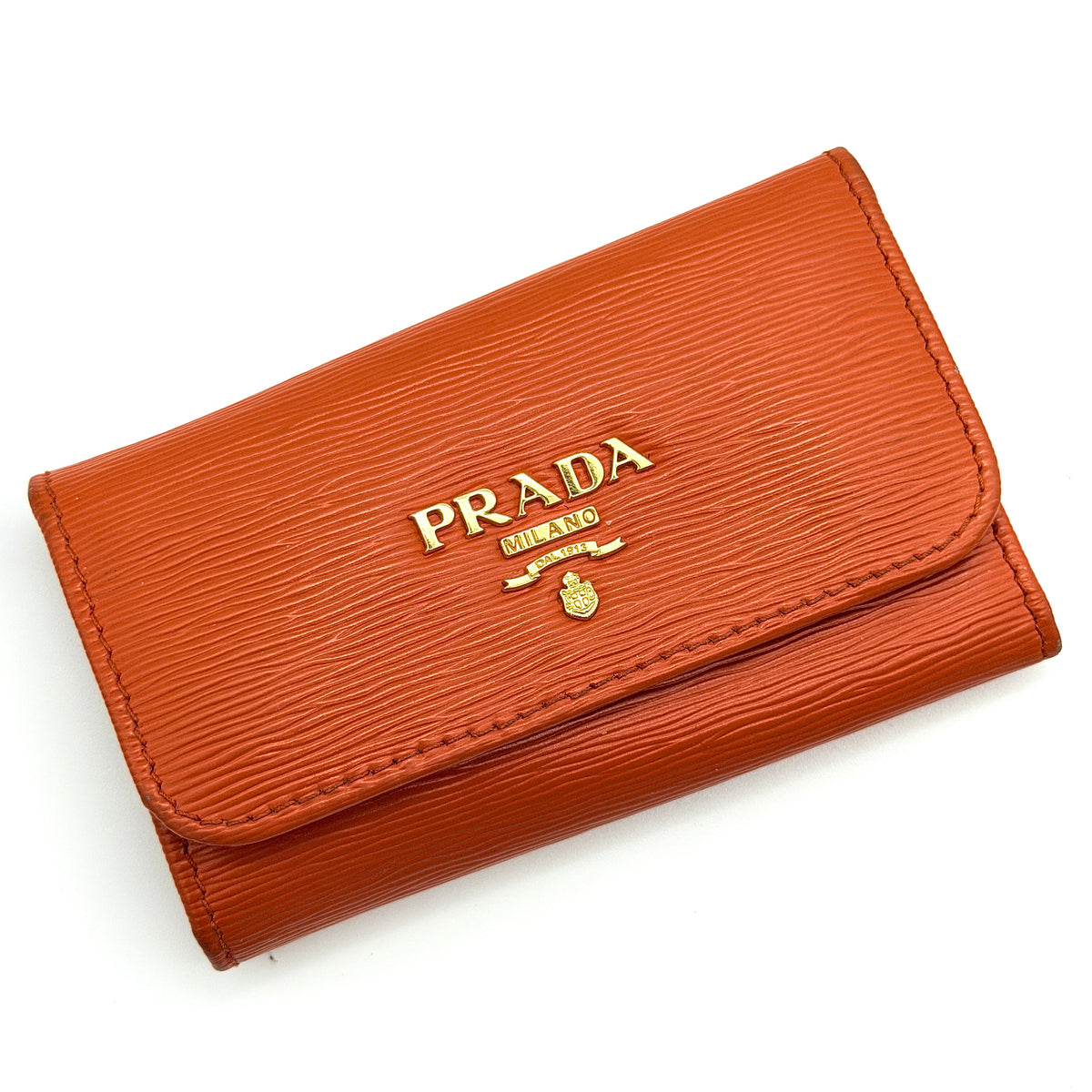 Prada Saffiano leather key case in orange with gold-toned hardware, Prada logo, and authenticity card displayed.