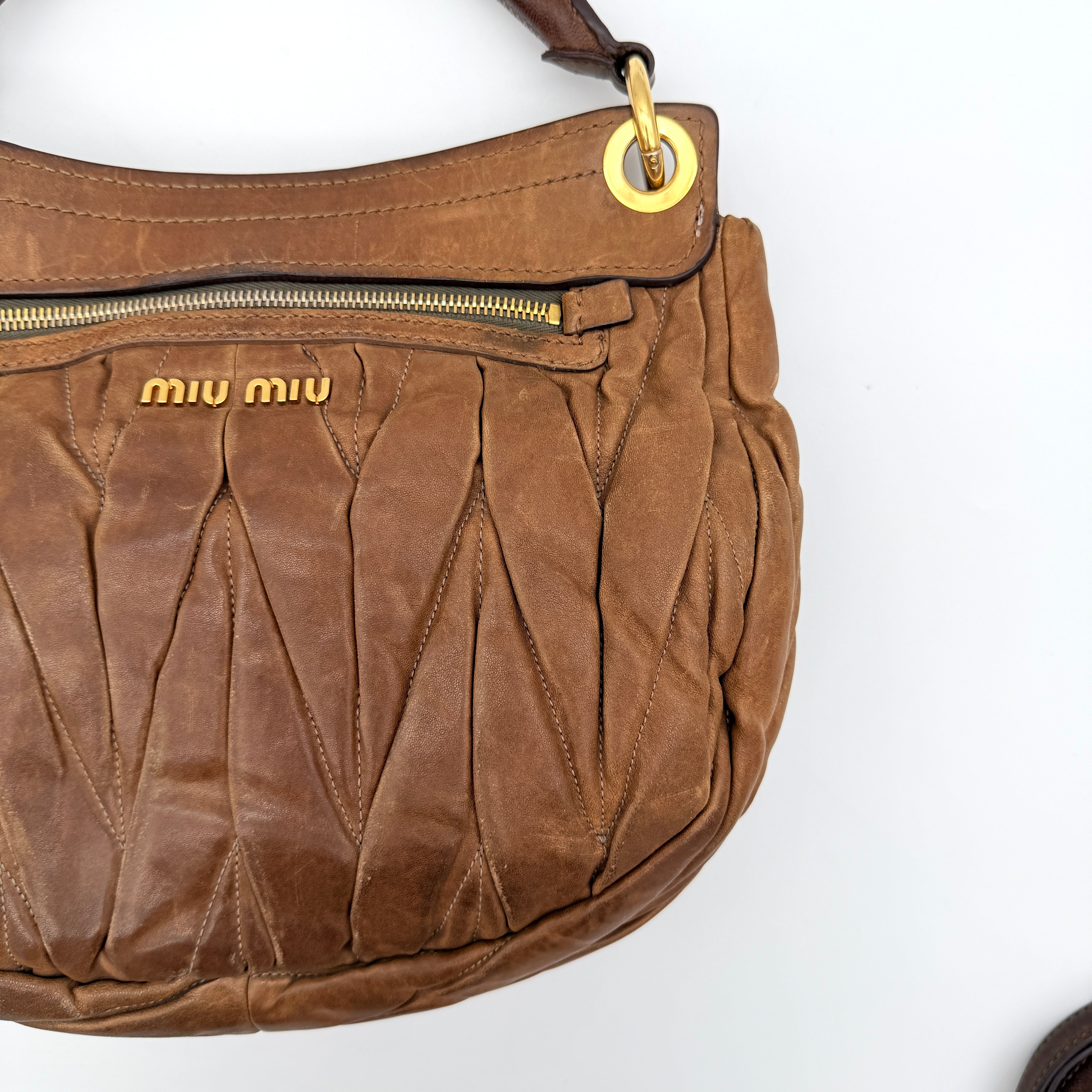 Miu Miu brown Matelasse Coffer Hobo bag with gold hardware, detachable strap, and dust bag displayed on a flat surface.