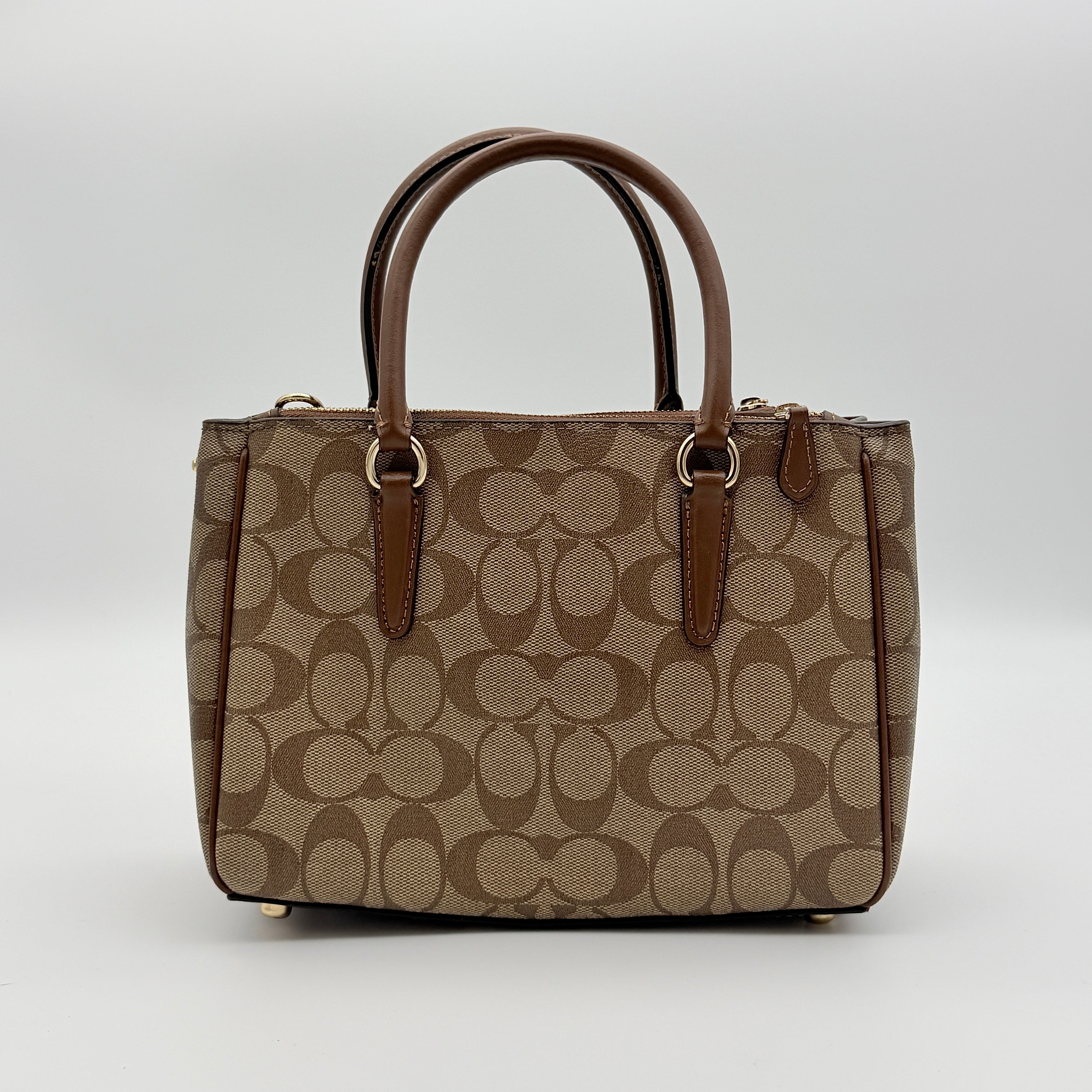 Coach Christie Carryall in beige and brown canvas with gold hardware and detachable strap, photographed in a studio setting.