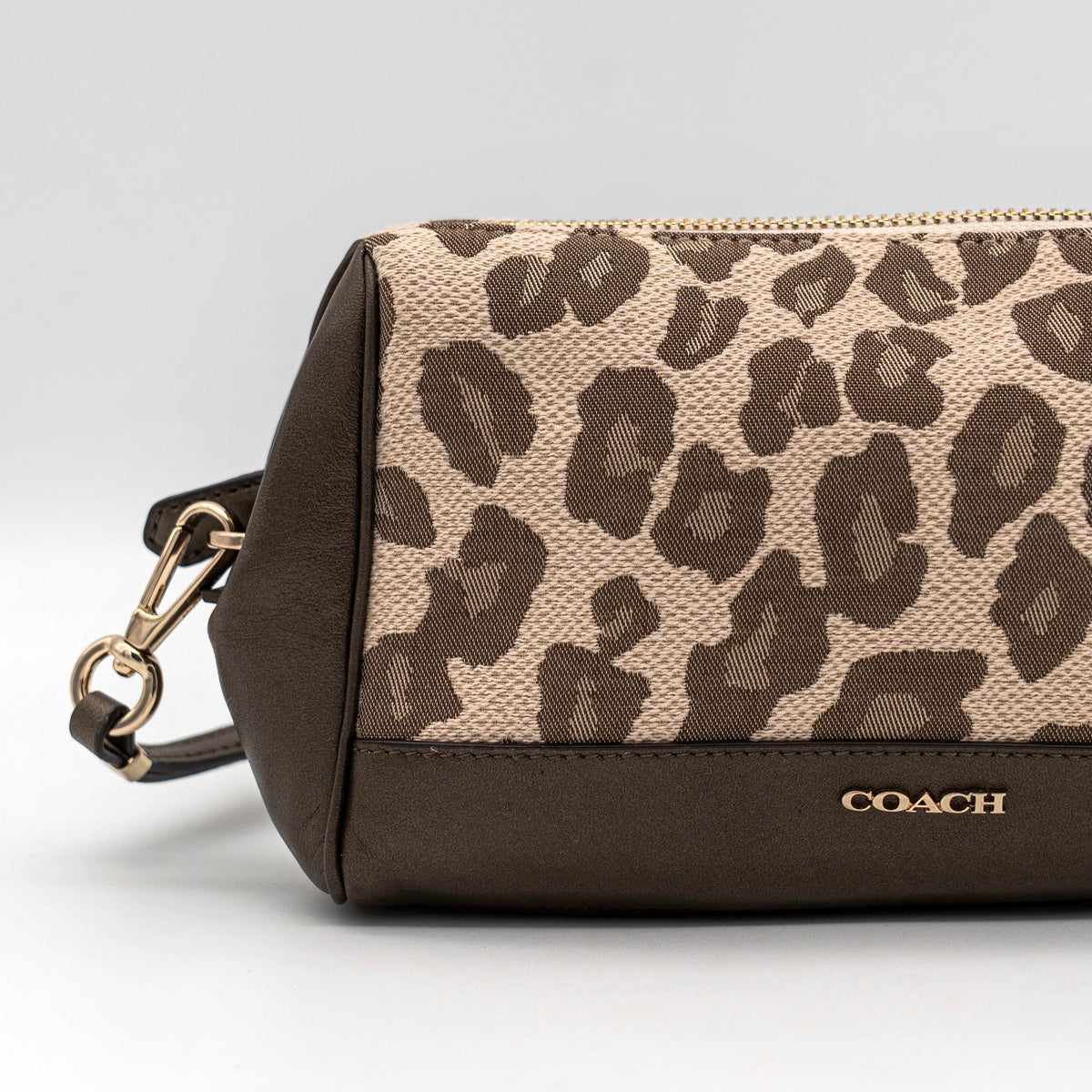 Coach cosmetic pouch in brown and beige leopard print canvas with chocolate leather trim and gold hardware, shown with wrist strap.