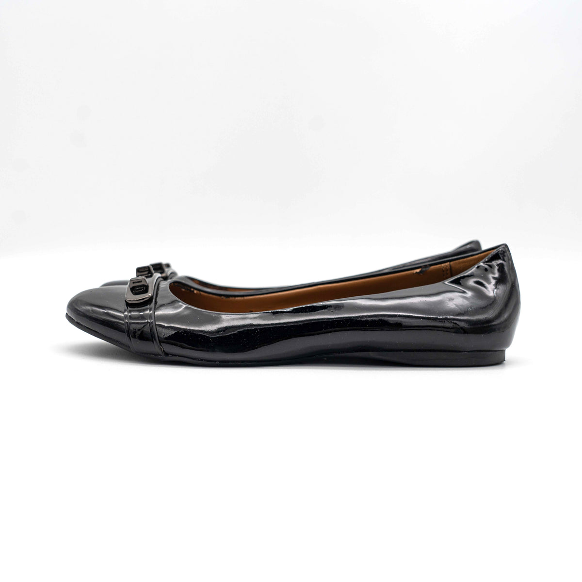 Coach Oswald Turnlock black patent leather ballet flats with dark metal hardware on the toe, photographed on a white background.