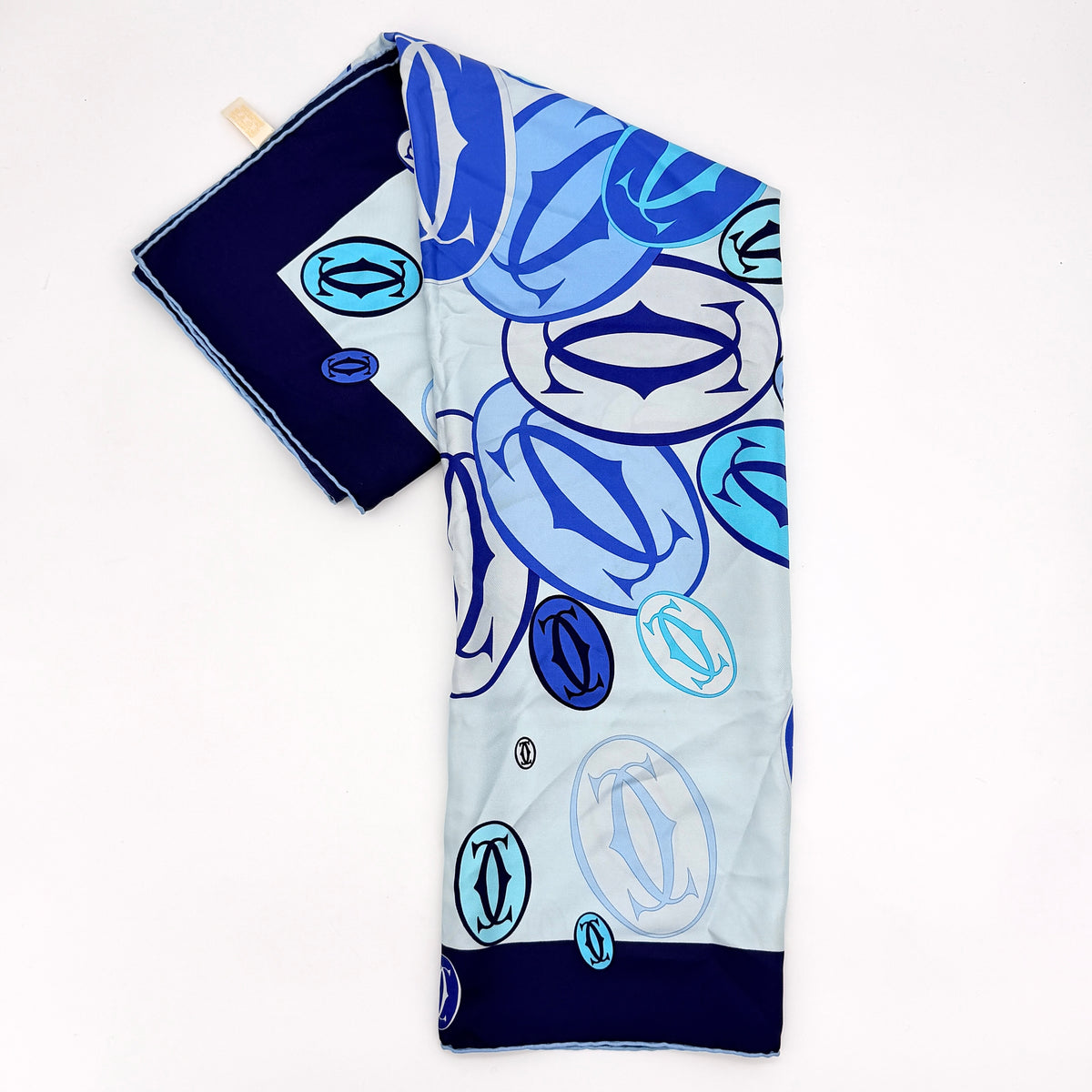 Cartier silk scarf in blue and white with graphic monogram logo print and navy border, elegantly arranged.
