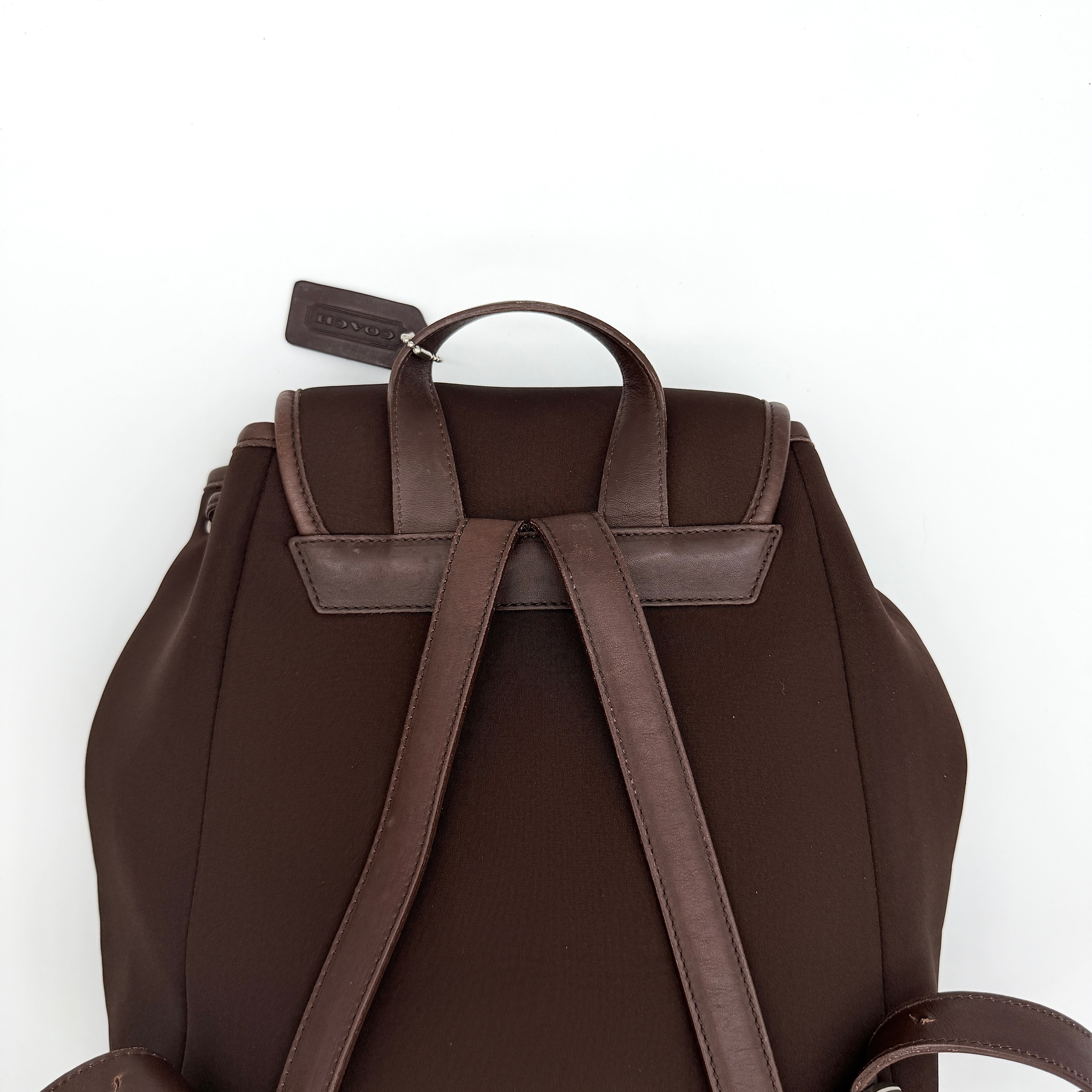 Coach brown neoprene drawstring backpack with leather trim, silver-tone hardware, and adjustable straps shown against a white background.