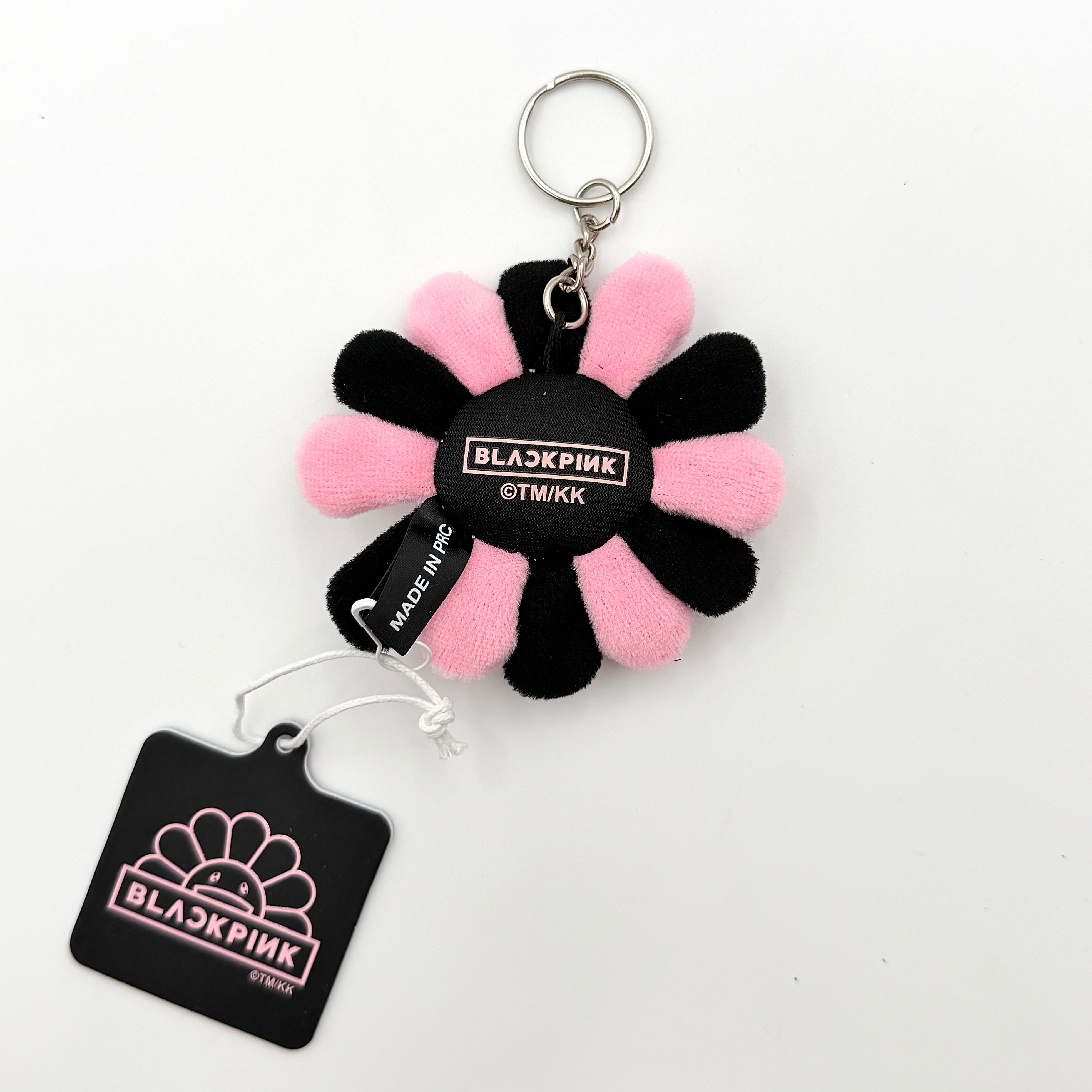 Takashi Murakami x BLACKPINK plush flower keychain in black and pink with smiling face and branded tag.