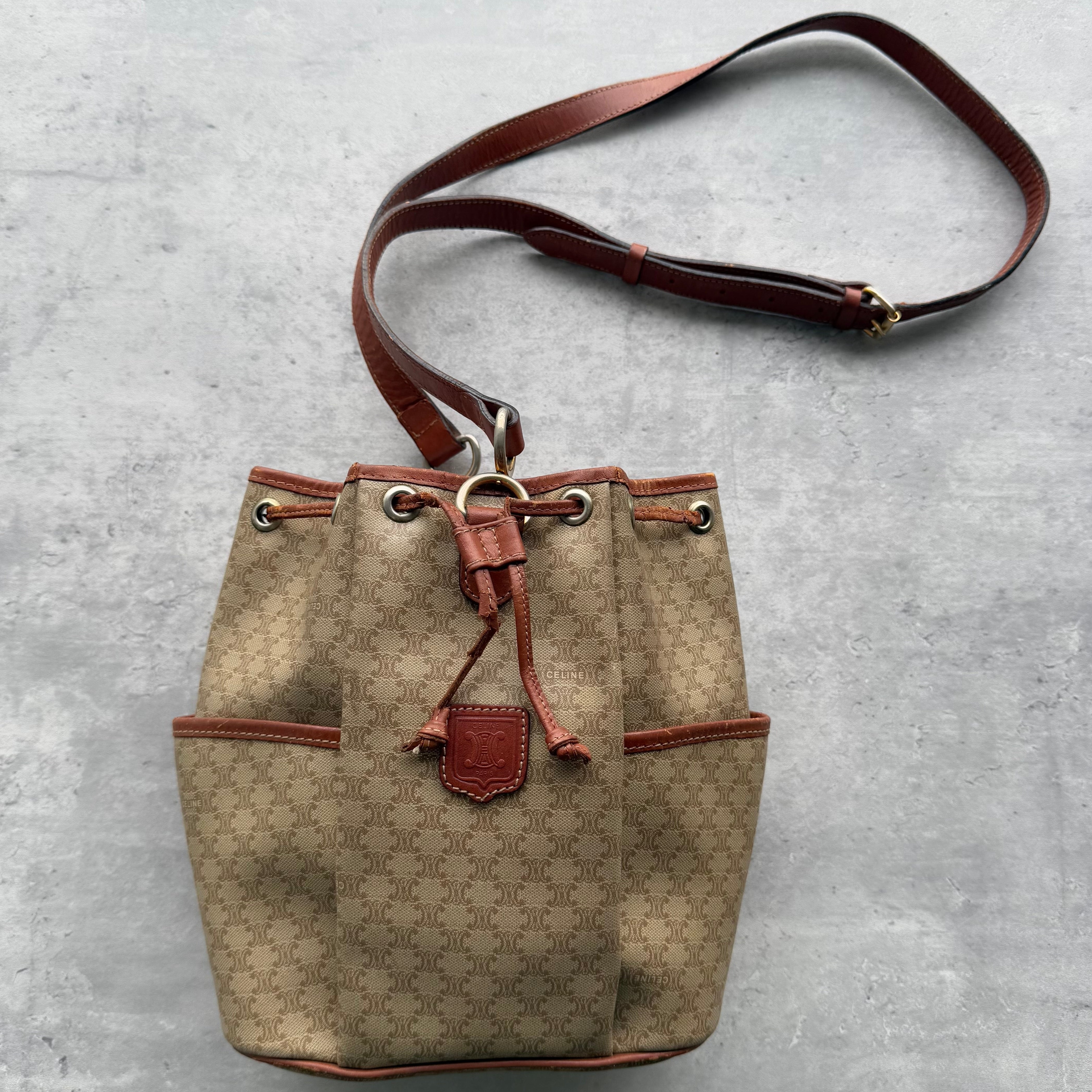Celine Macadam Bucket Drawstring Bag in beige canvas with brown leather trim, gold-tone hardware, and adjustable shoulder strap.