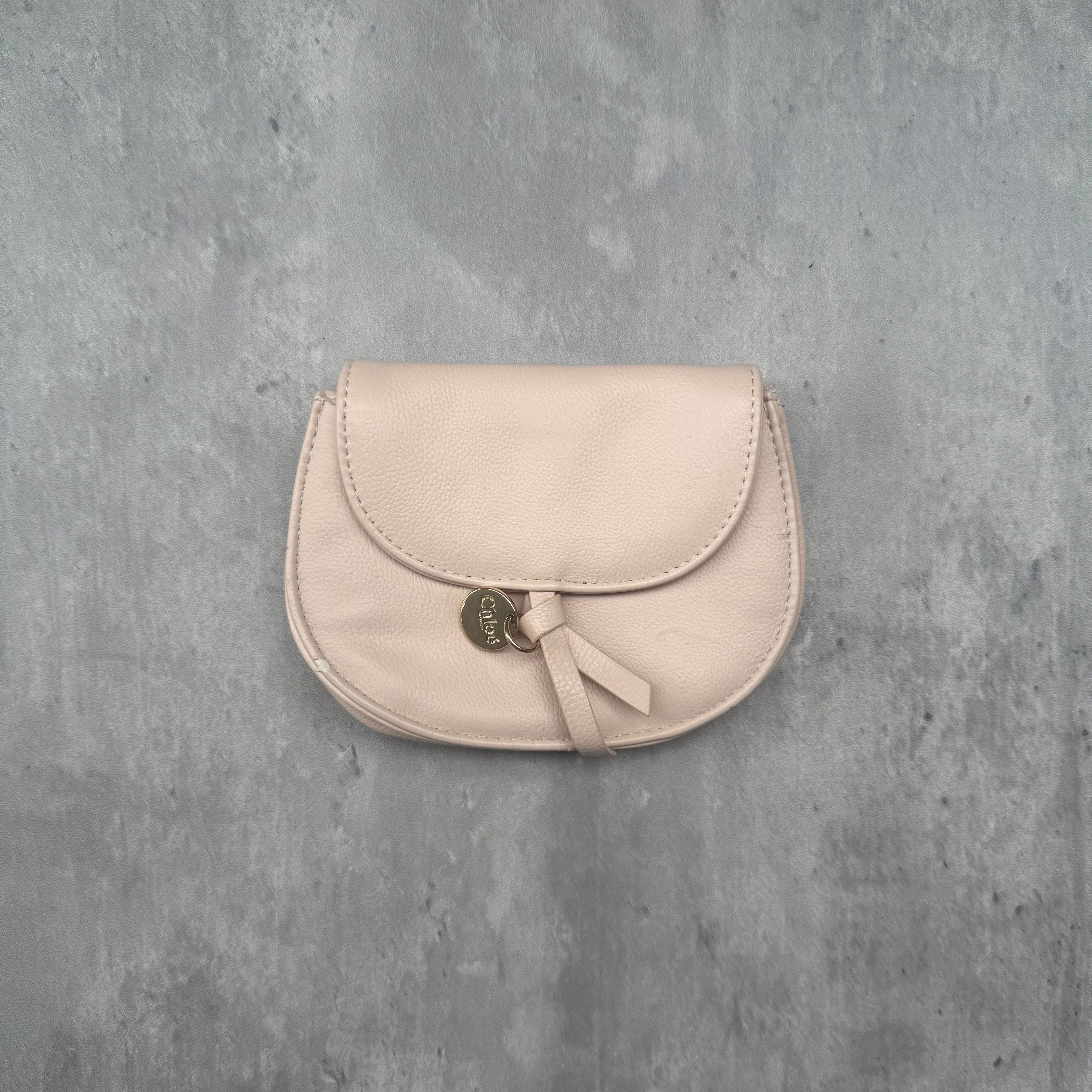 Shop the Chloé Charm Pouch Wallet in light pink, featuring pebbled leather, a Chloe charm, and a suede interior. A pre-loved luxury accessory available now at Elevated Studios.