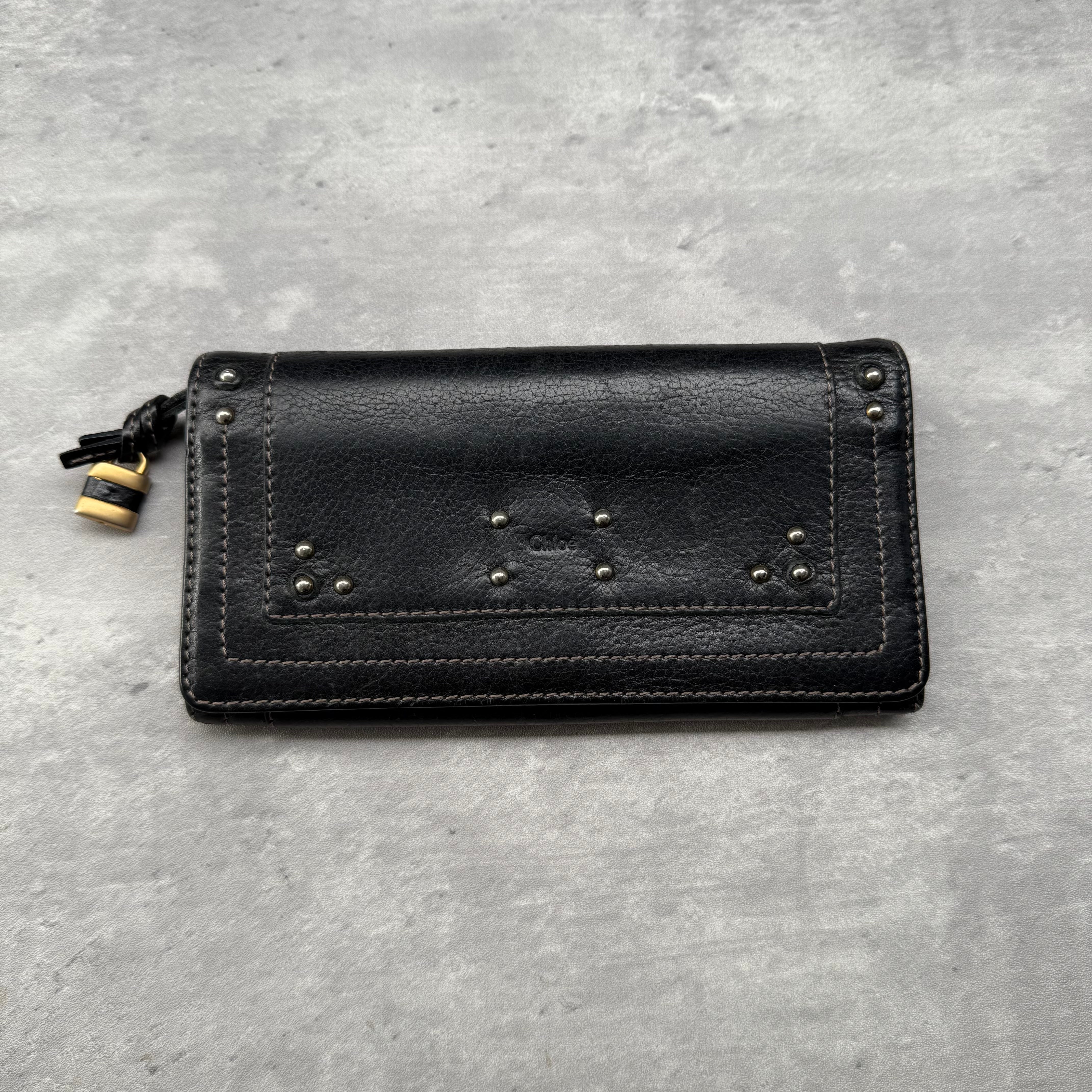 Chloé Paddington Long Wallet in black grained leather with gold-tone padlock and stud accents, featuring card slots, ID window, and zippered compartment.