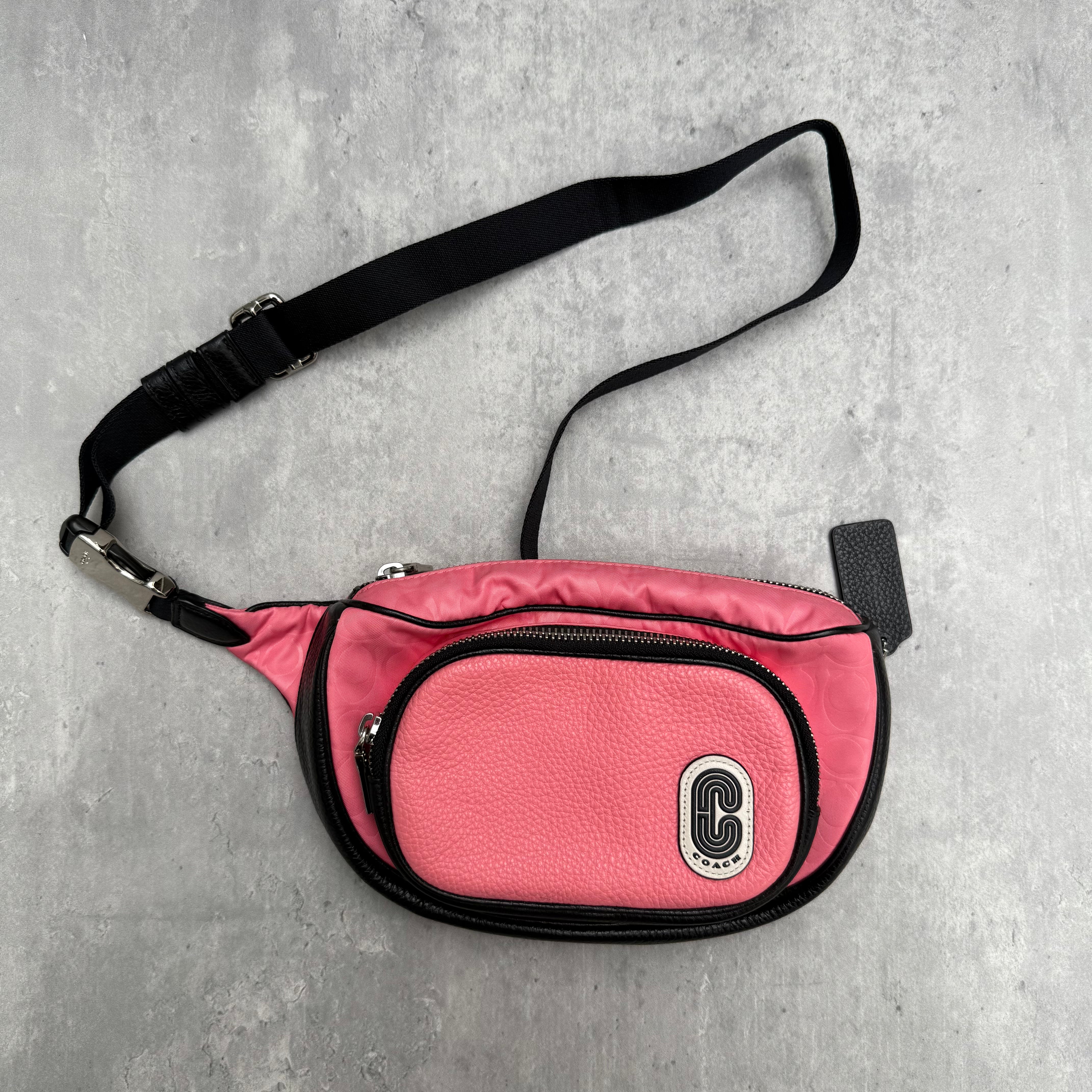 Coach Court Belt Bag in pink pebbled leather with black trim, oval logo plaque, and adjustable strap.