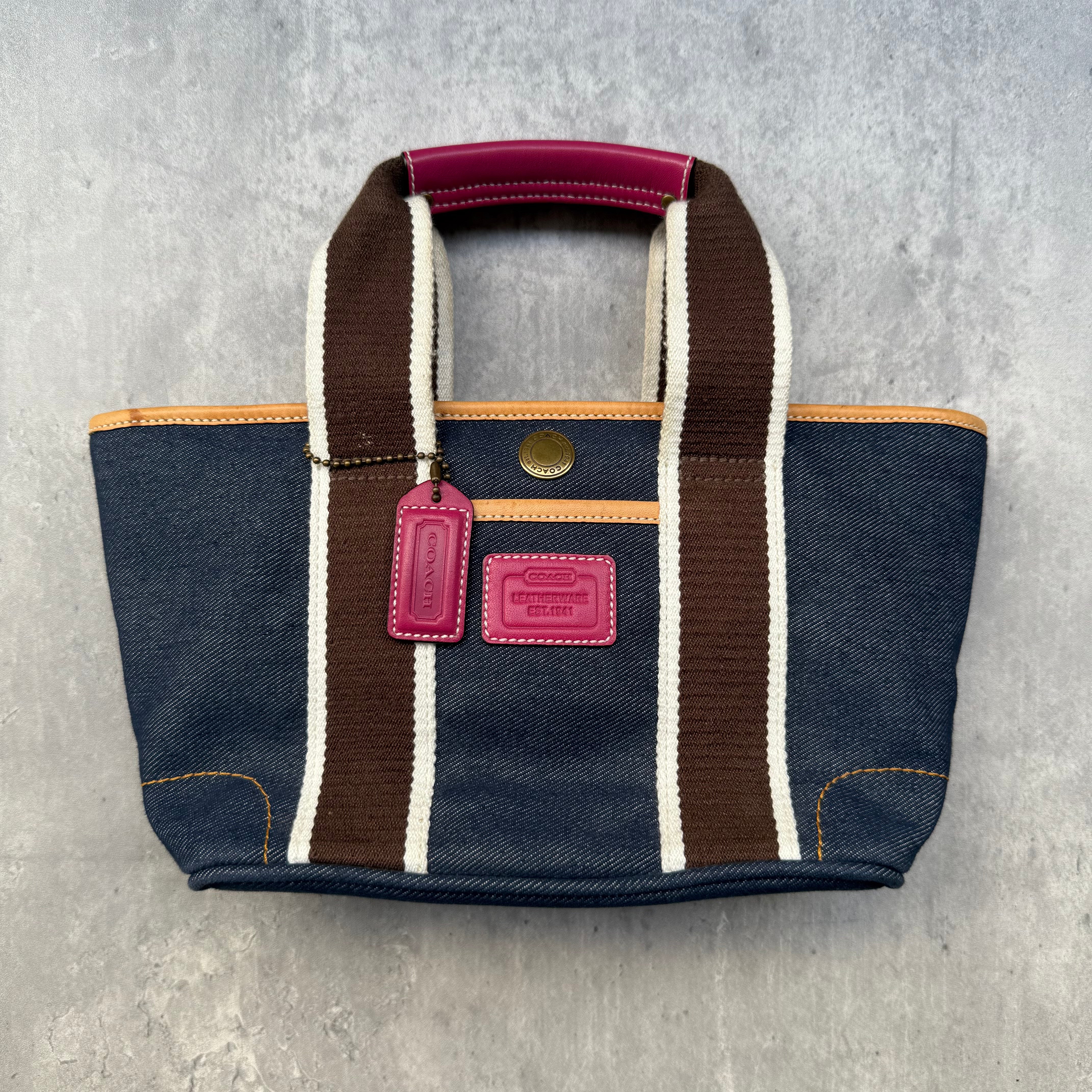Coach Denim Hampton Mini Tote Bag in denim with brown and white webbed handles, pink leather hangtag, and orange accents.