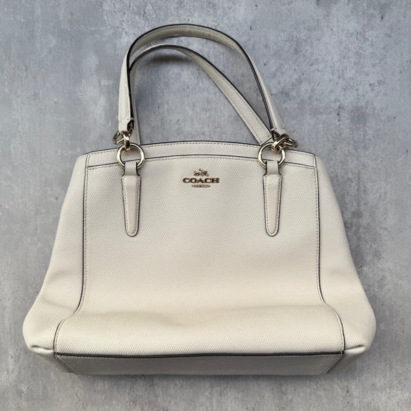  Coach Minetta Handbag in white pebbled leather with structured silhouette, top handles, and gold-tone logo