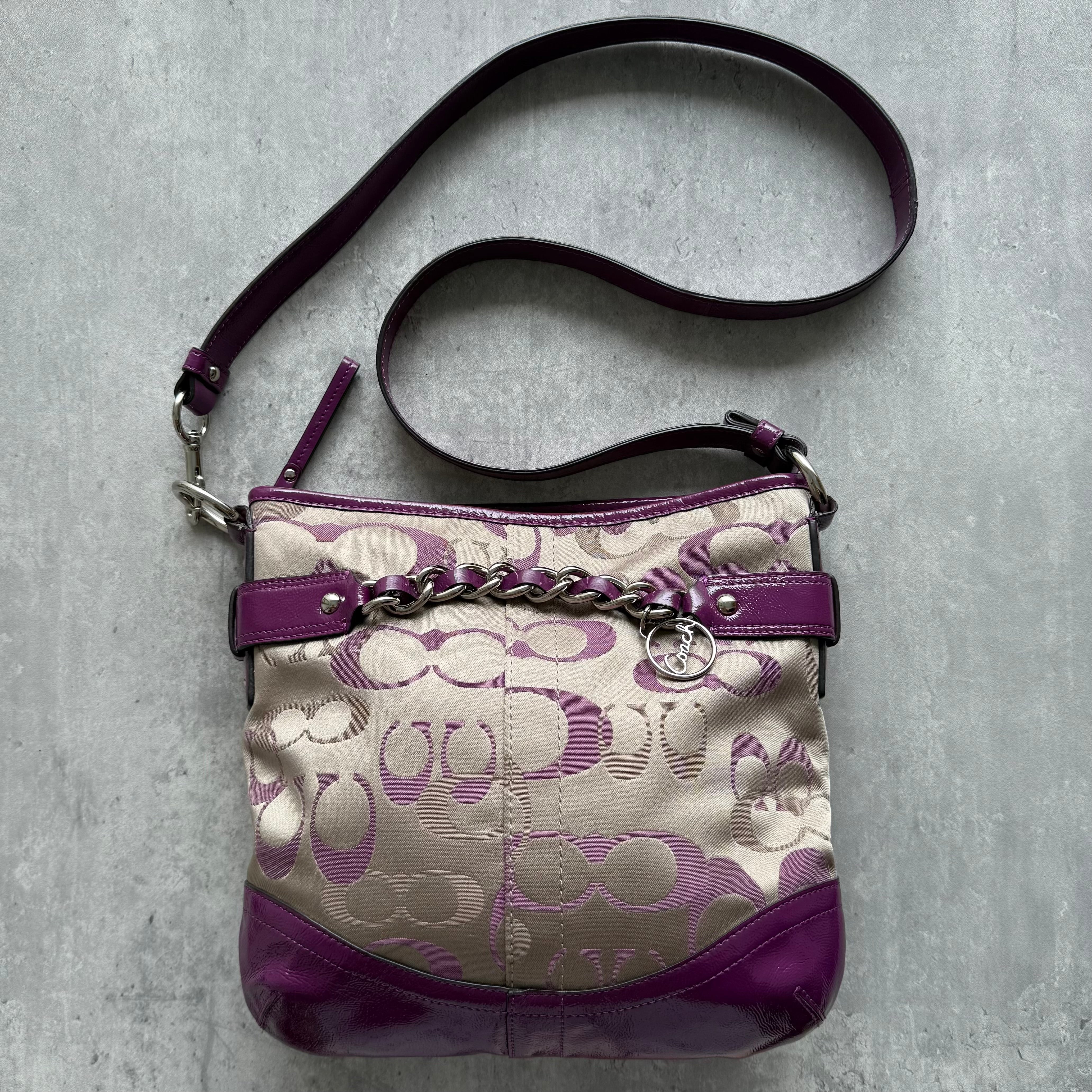 Coach Signature Canvas Crossbody Bag in beige with purple leather trim, chain detail, and adjustable strap.