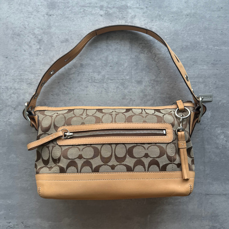 Coach Signature East West Shoulder Bag in beige monogram canvas with tan leather trim, silver hardware, and grommet-detailed strap.