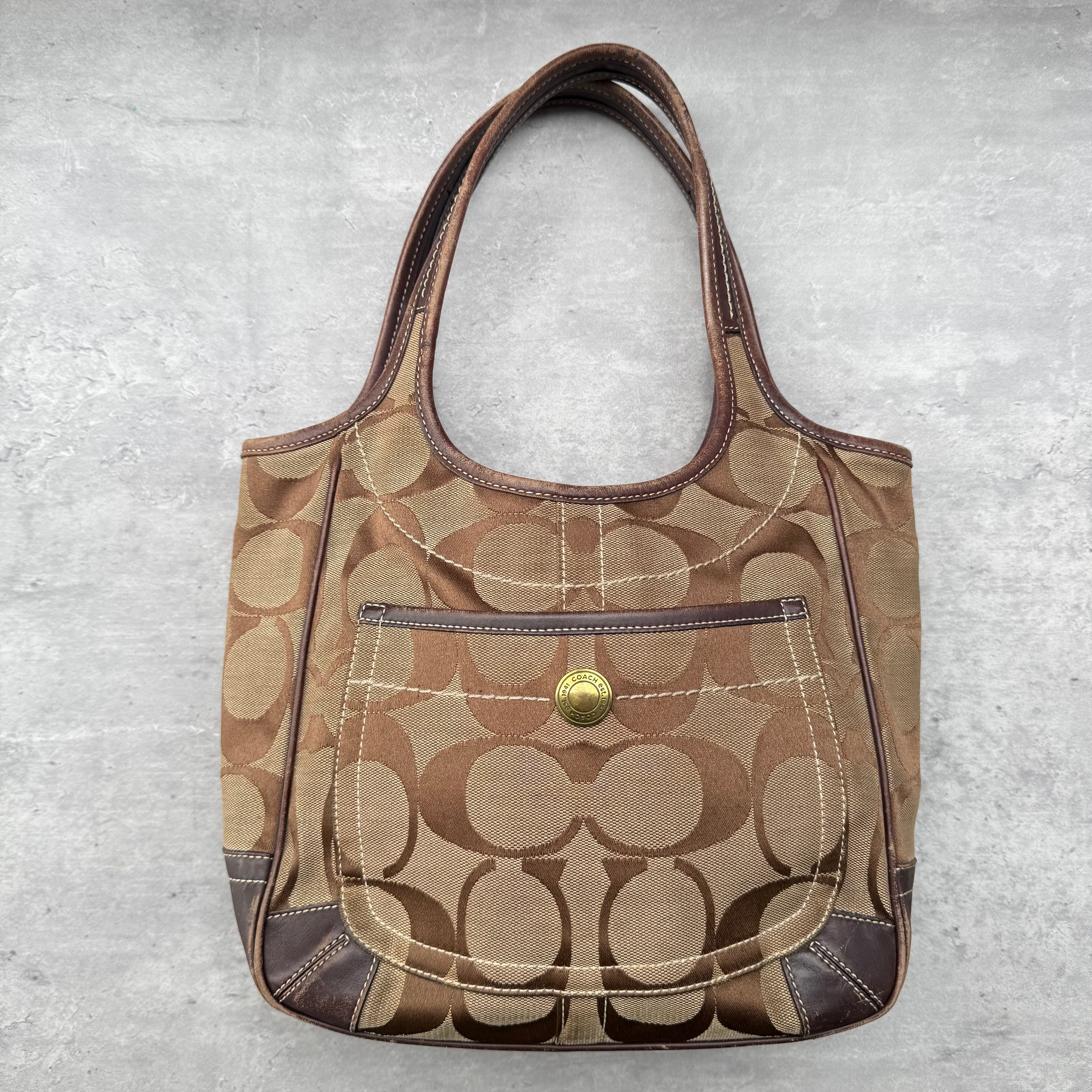 Coach Signature Ergo Tote Bag in brown and beige monogram canvas with front snap pocket and leather trim.
