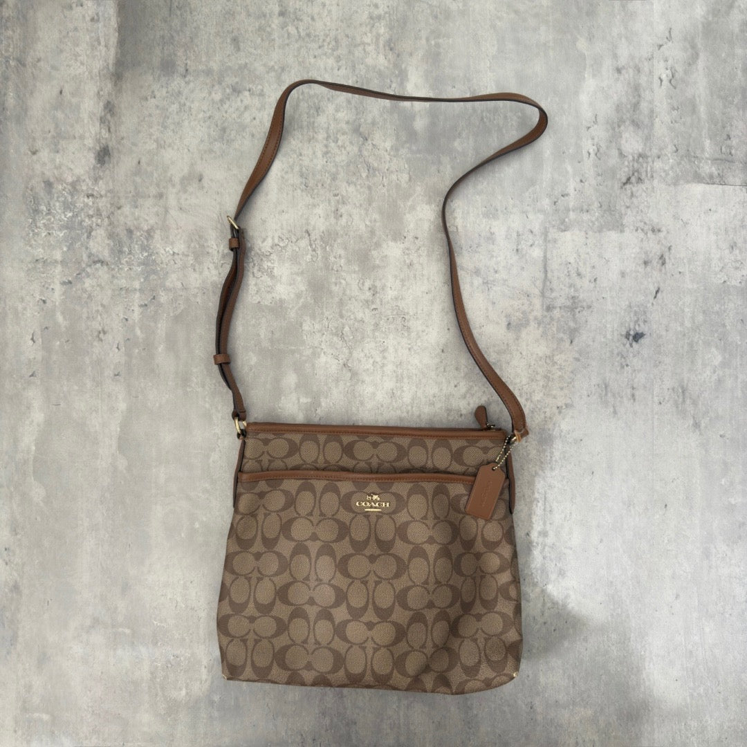 Coach Signature File Crossbody Bag in beige and brown monogram canvas, featuring leather trim, gold-tone hardware, and an adjustable crossbody strap.