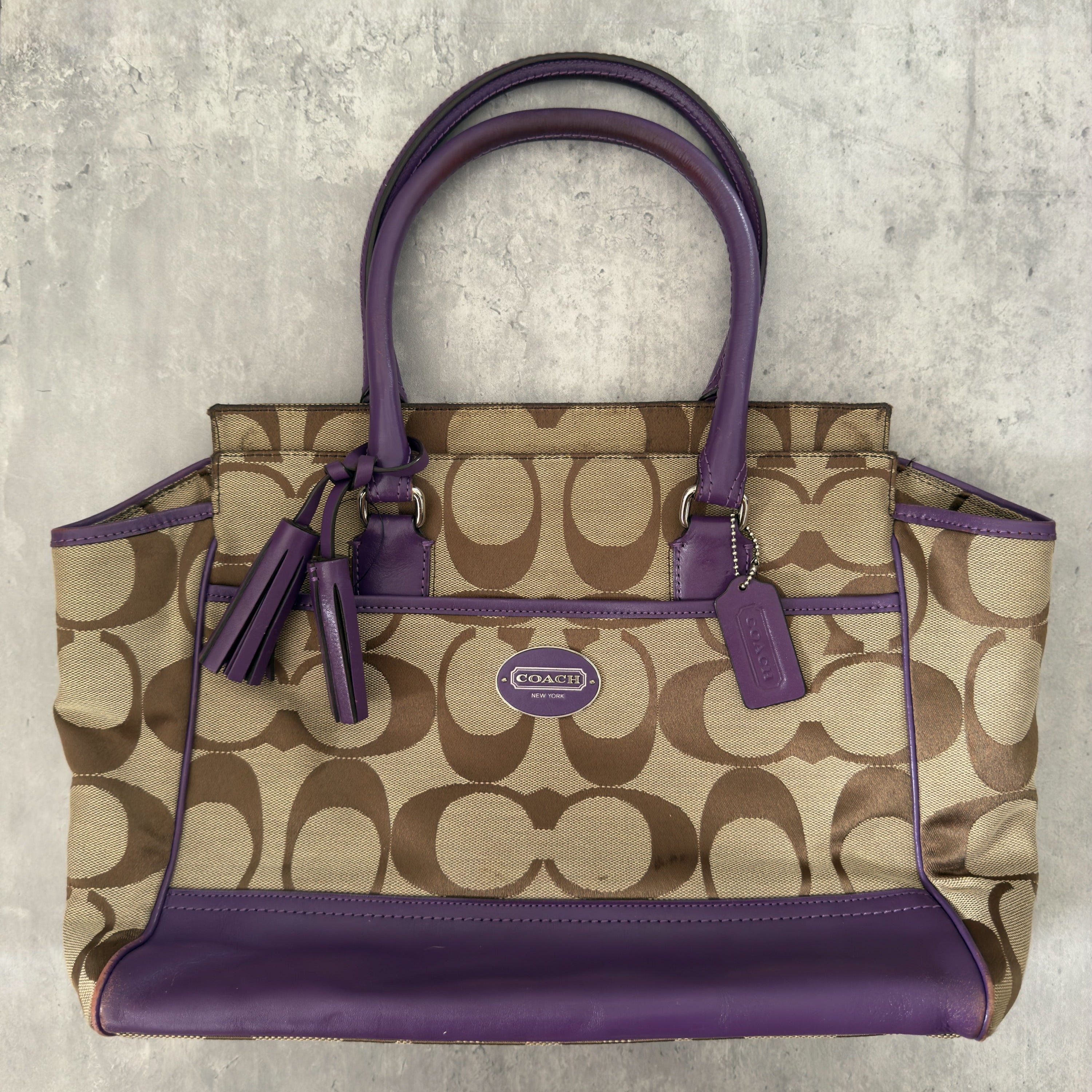 Coach Signature Legacy Candace Carry-All handbag in beige coated canvas with monogram print, purple leather trim, silver-tone hardware, and tassel details.
