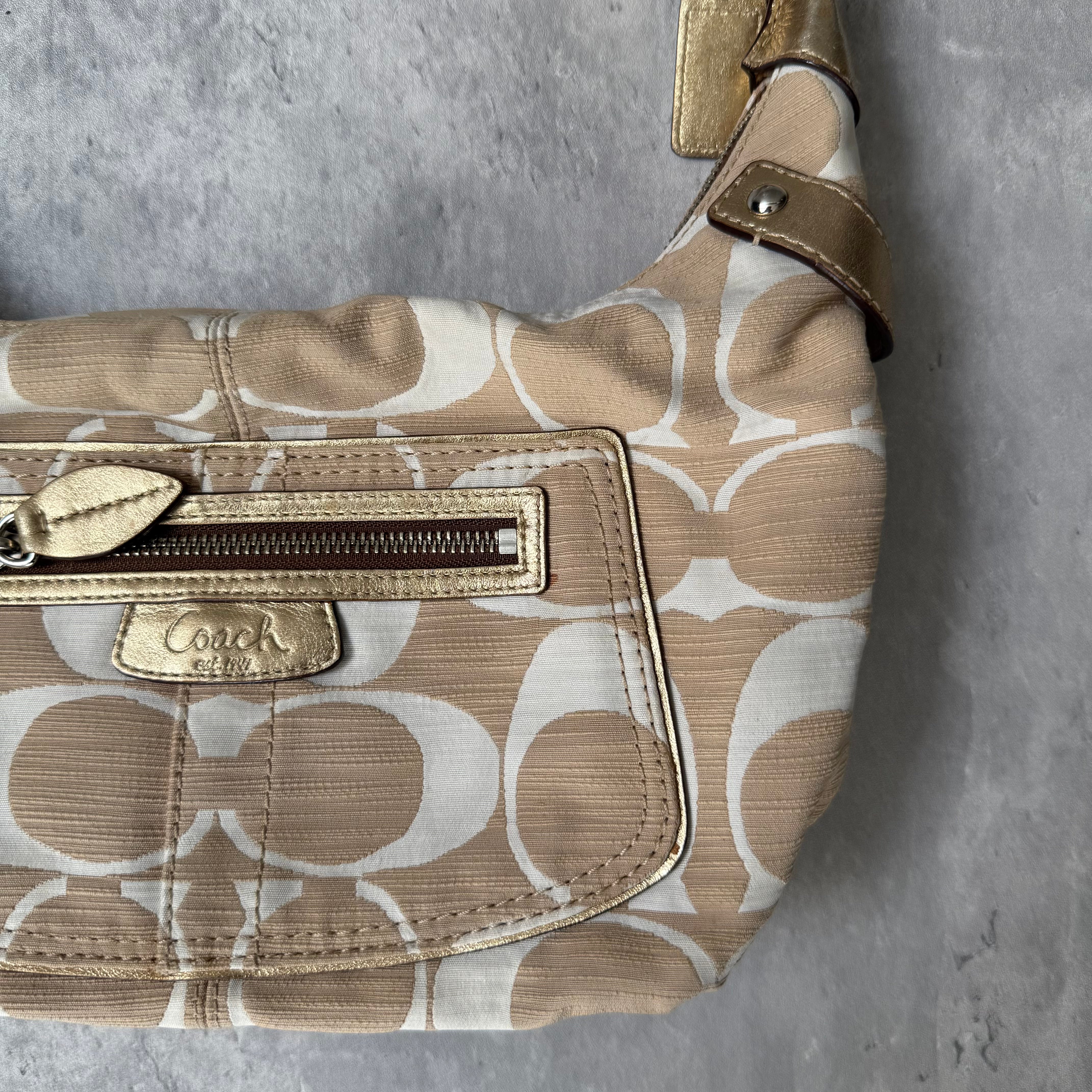 Coach Signature Penelope Hobo Shoulder Bag in beige and white canvas with metallic trim, front zip pocket, and silver-tone hardware.