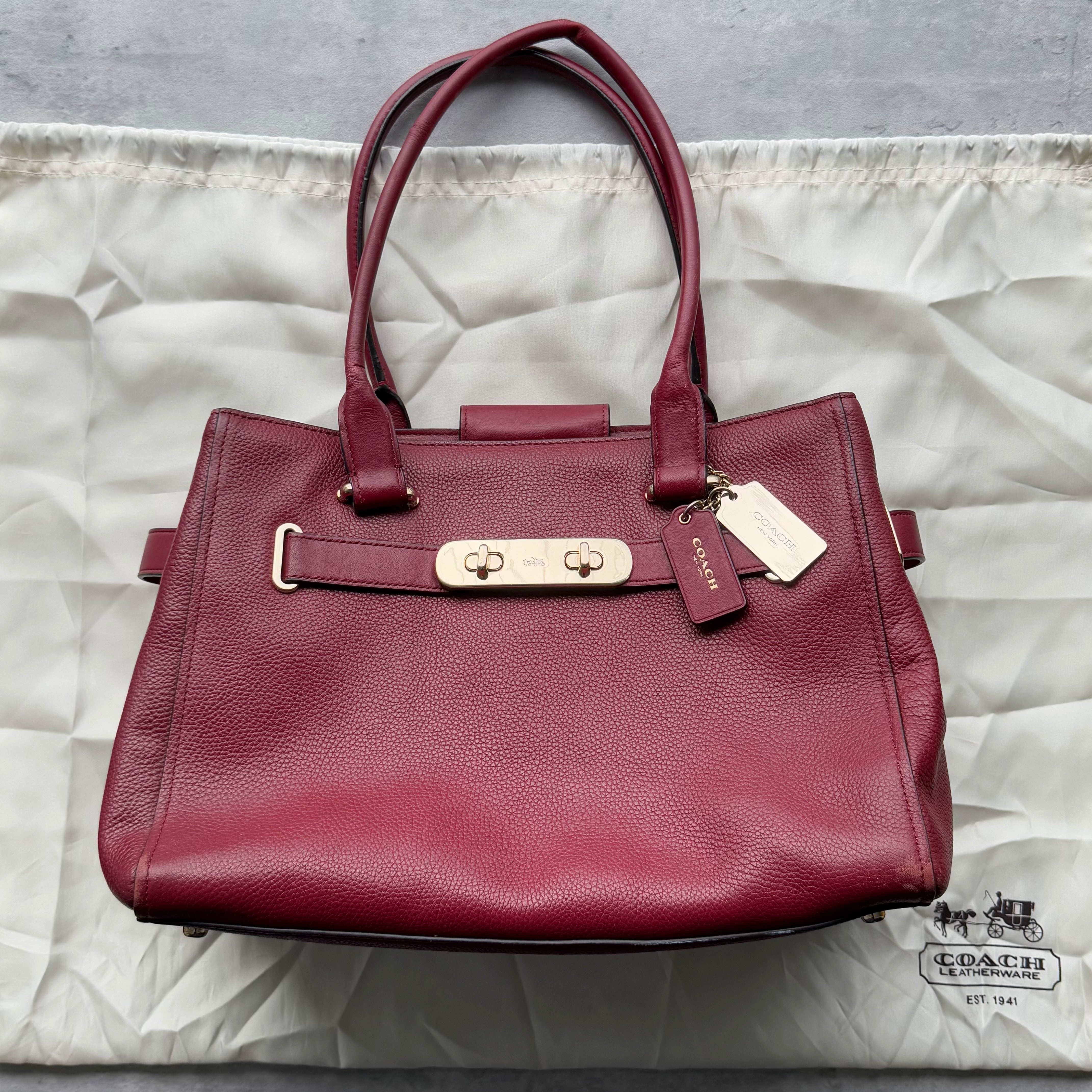 Coach Swagger Carryall Handbag in burgundy pebbled leather with gold-tone hardware, dual top handles, and spacious divided interior.