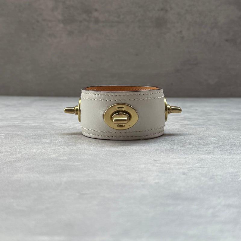 Coach Turnlock Cuff Bracelet White, crafted in white leather with gold-tone turnlock hardware and tan leather lining.
