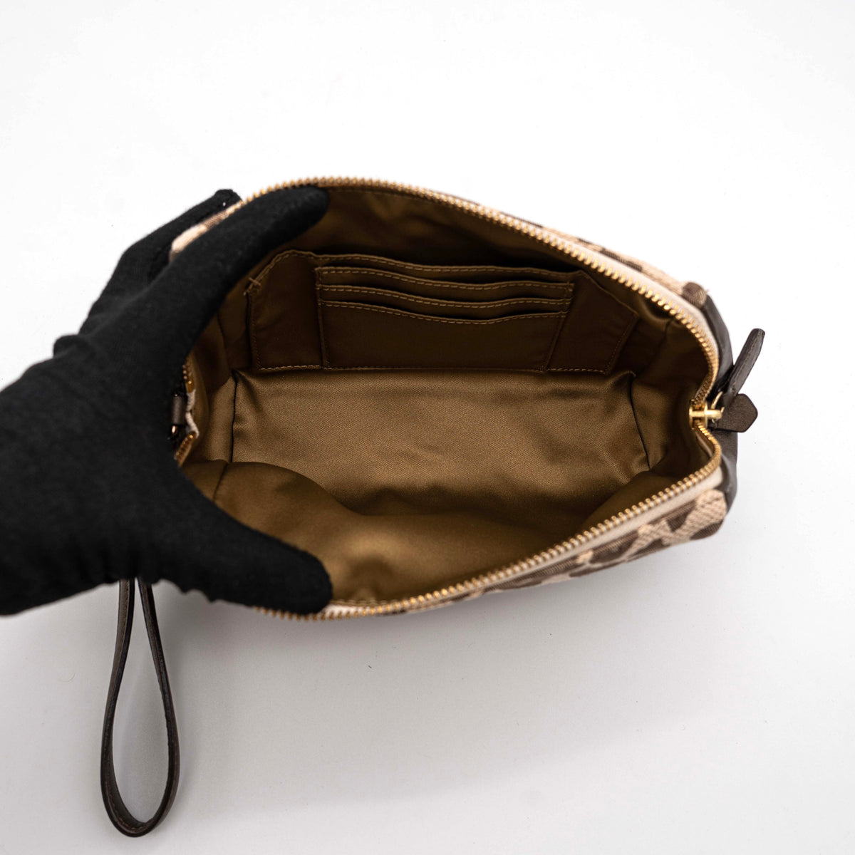 Coach cosmetic pouch in brown and beige leopard print canvas with chocolate leather trim and gold hardware, shown with wrist strap.