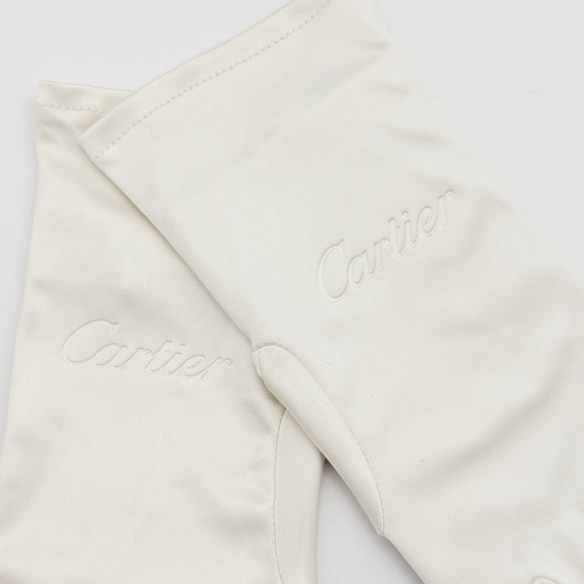 Pair of Cartier ivory gloves with signature script logo embroidery displayed on a flat white background.