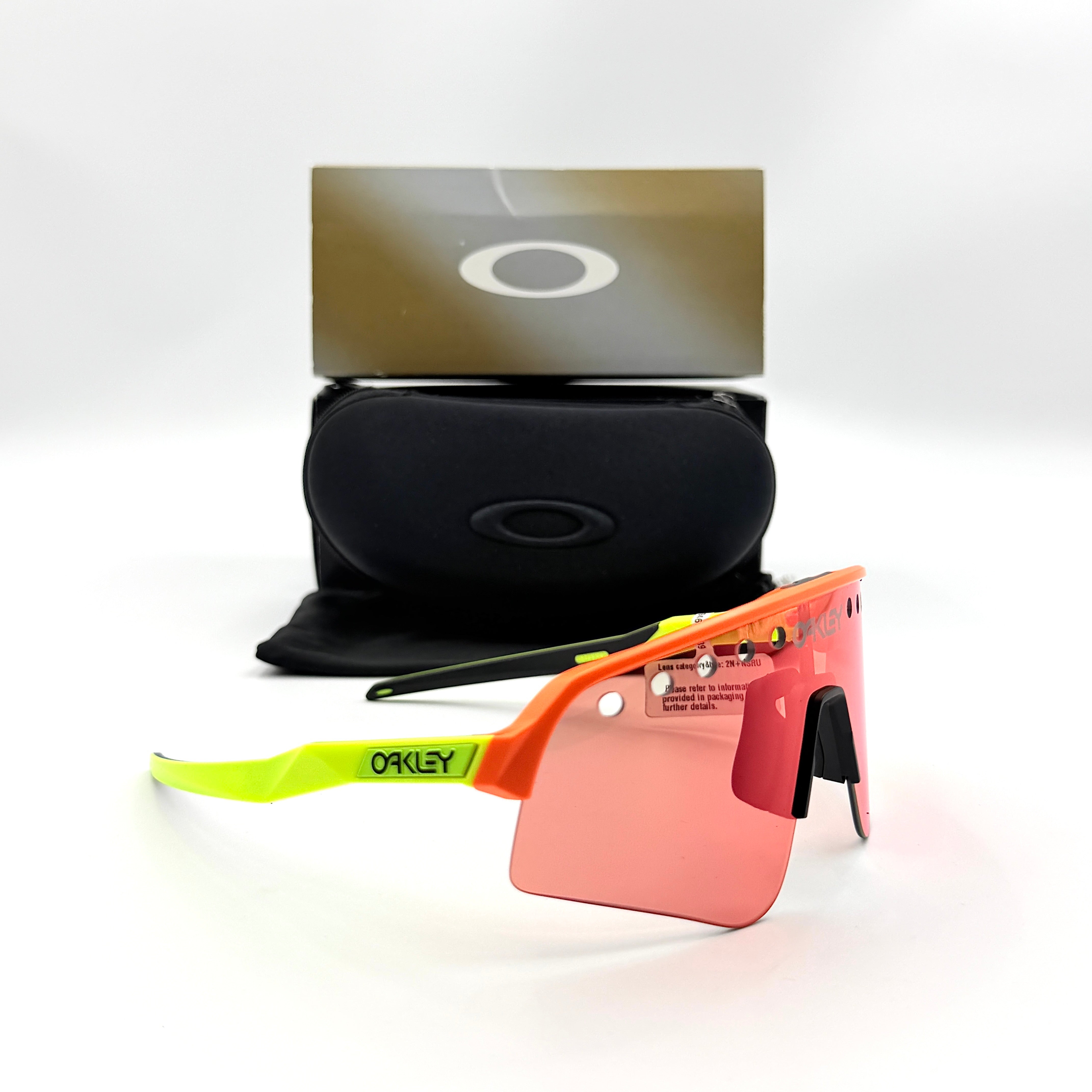 Oakley Sutro Lite Sweep sunglasses in neon yellow and orange with Prizm Trail Torch shield lens, displayed with box and case.