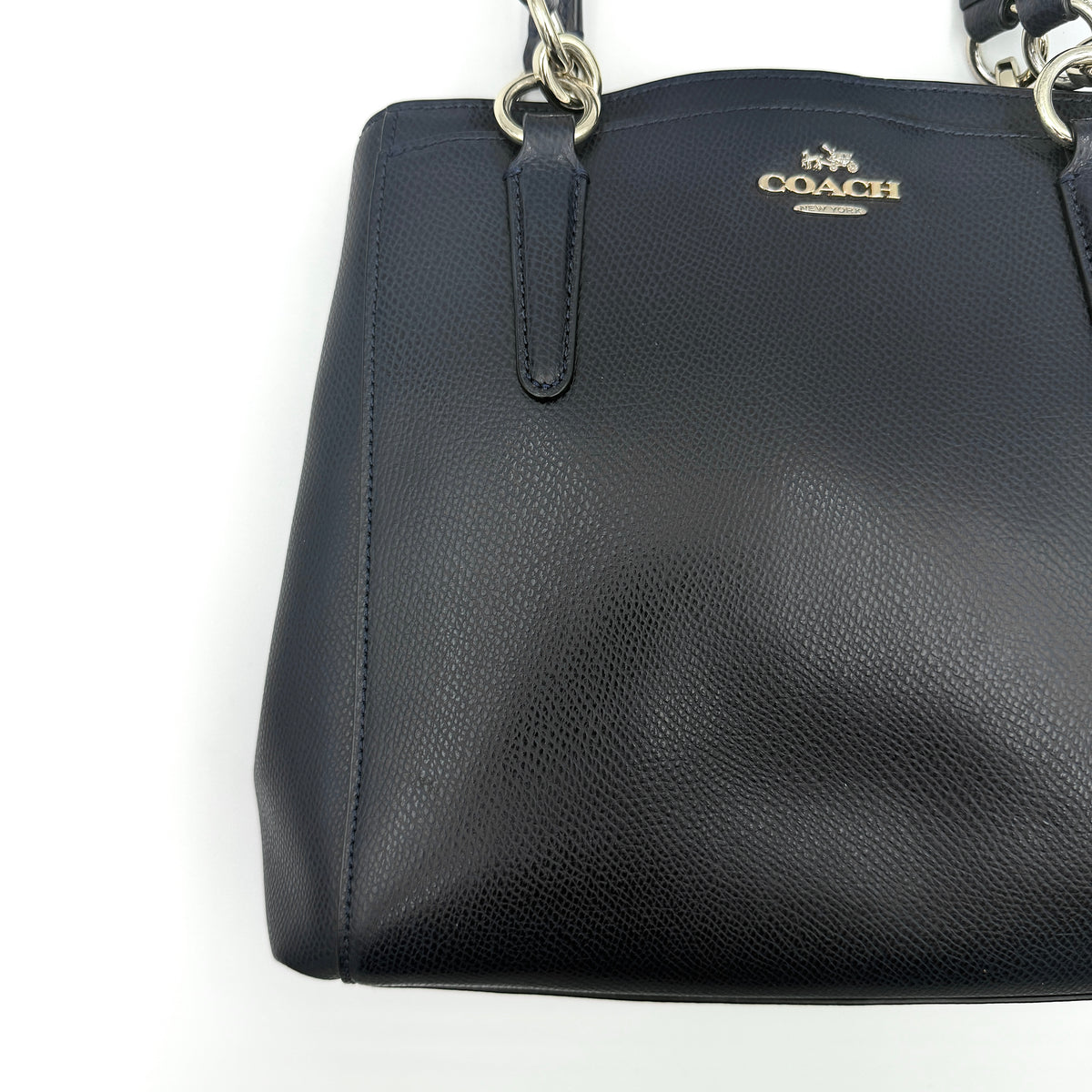 Coach Minetta Satchel in navy blue grained leather with dual handles and detachable shoulder strap displayed on a white background.