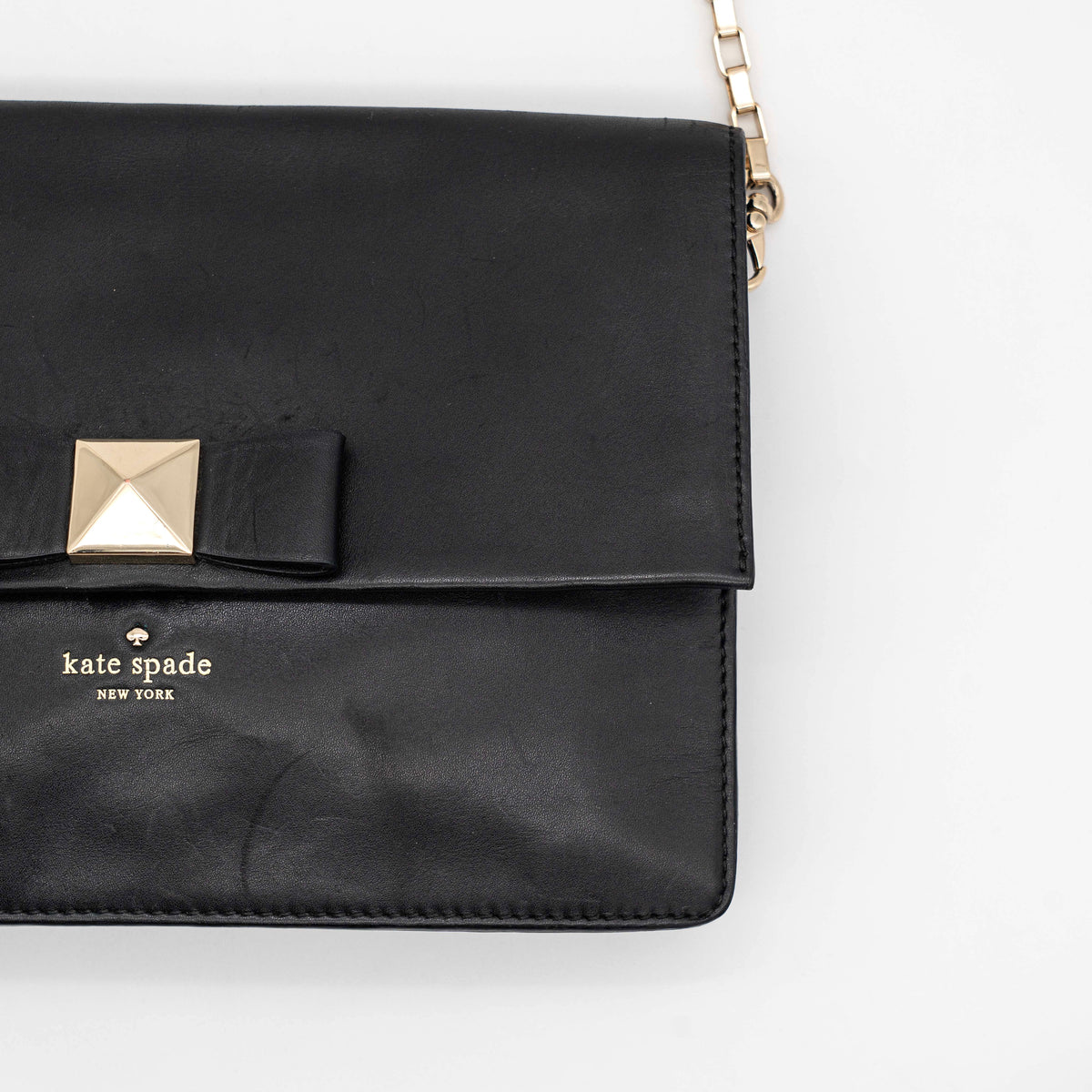 Kate Spade New York black leather shoulder bag with gold chain strap and bow detail, displayed against a white background.