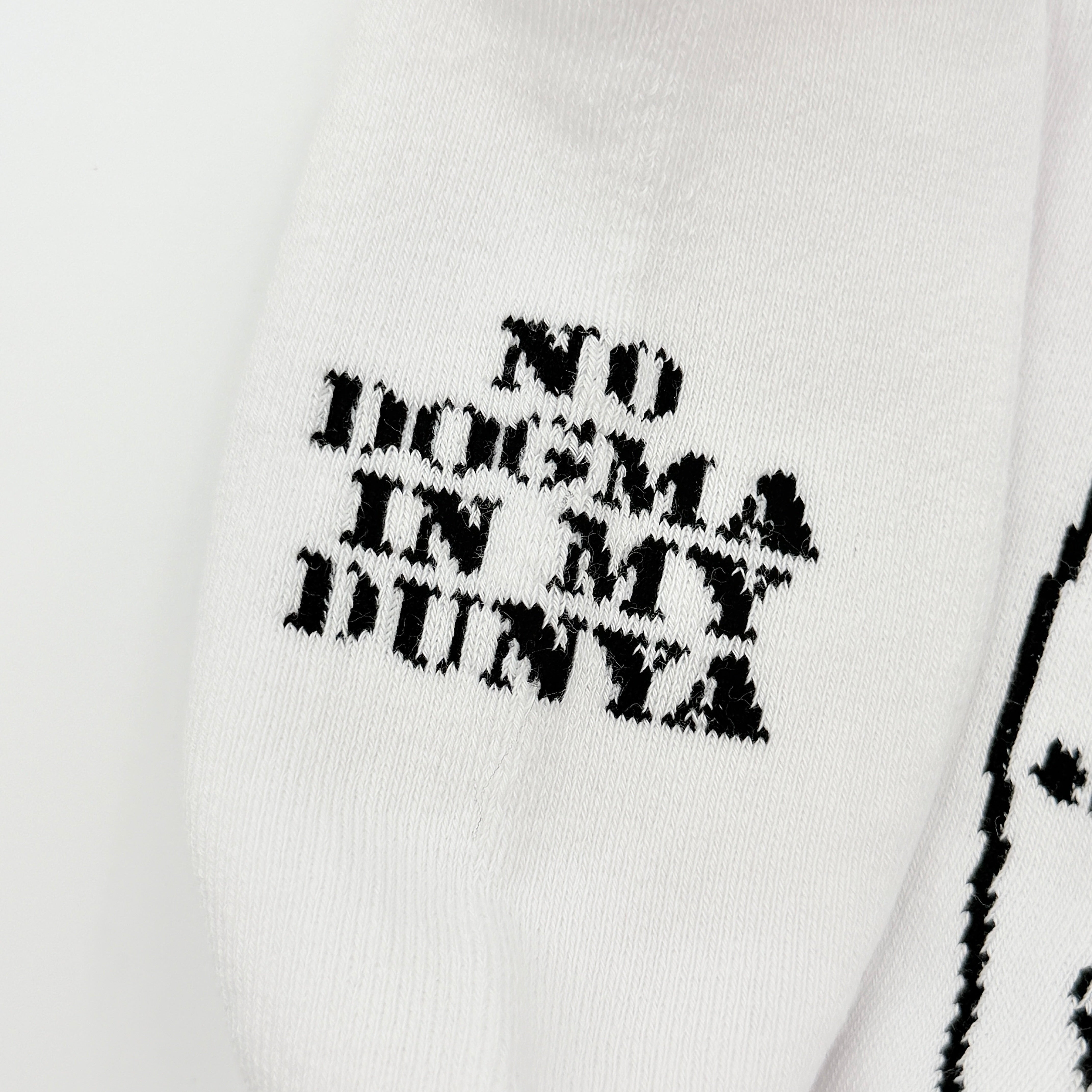 A pair of Corteiz Alcatraz white socks with black logo on the ankle and statement text on the sole.