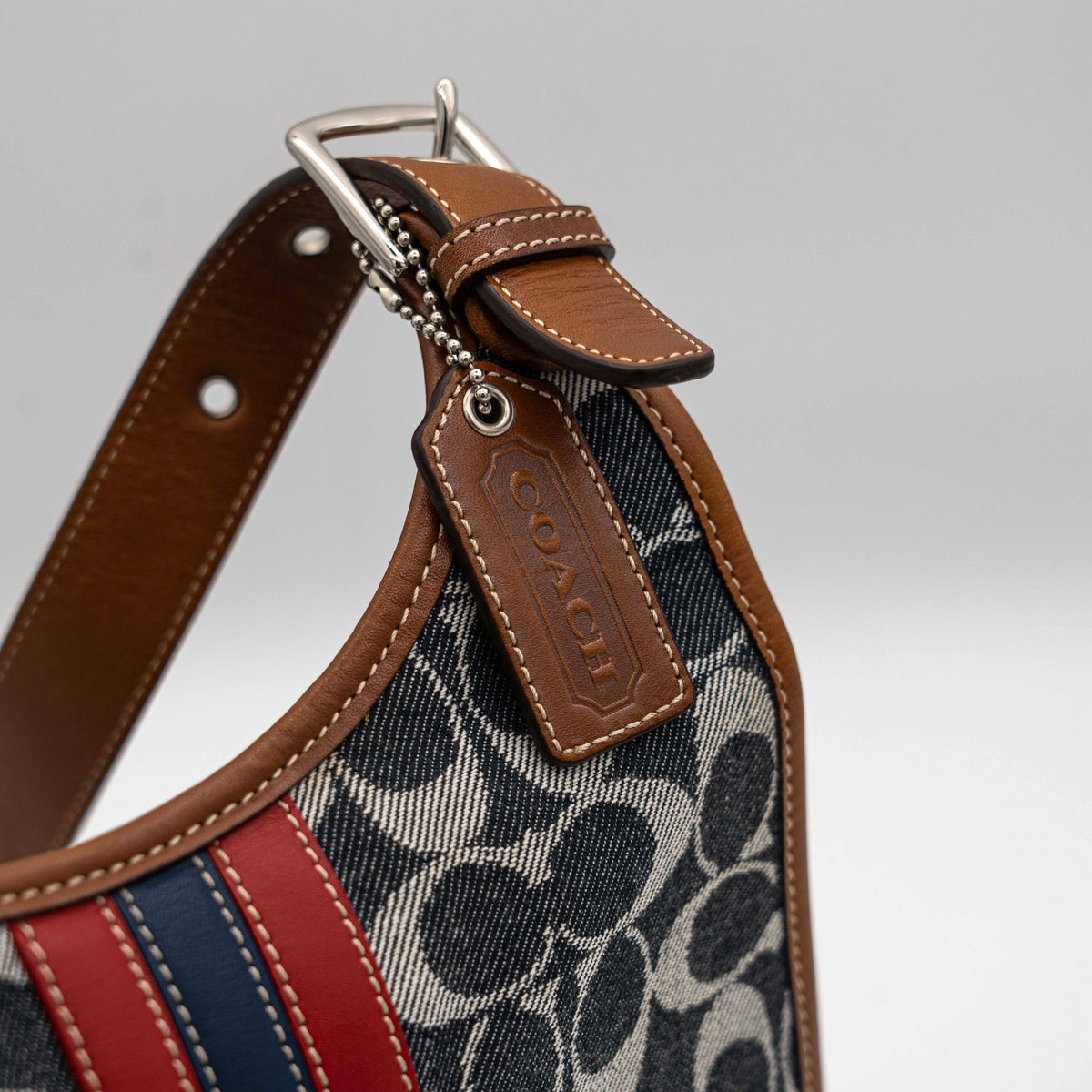 Coach signature denim hobo crossbody bag with red and blue stripe, brown leather trim, and an adjustable strap.