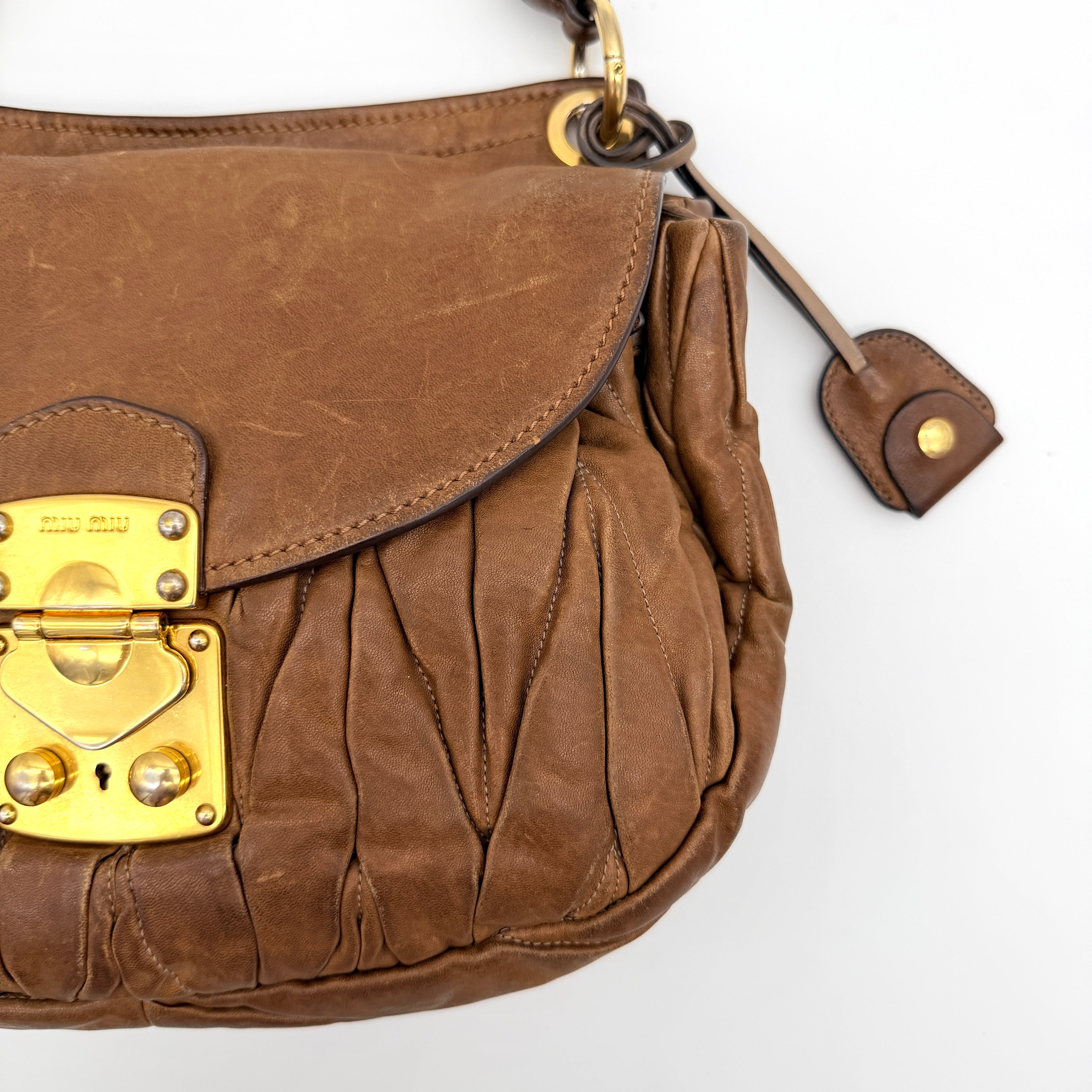 Miu Miu brown Matelasse Coffer Hobo bag with gold hardware, detachable strap, and dust bag displayed on a flat surface.