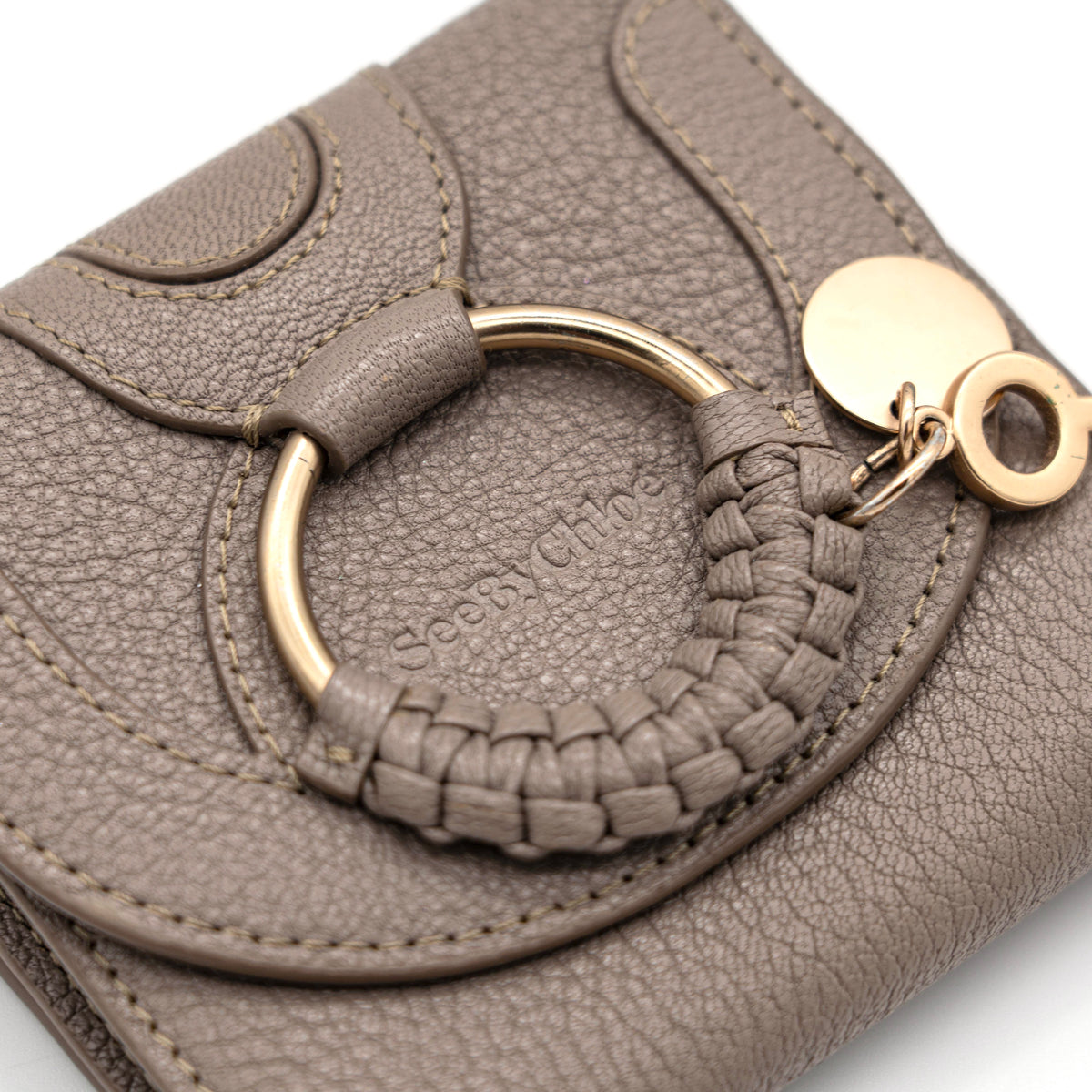 See by Chloe Hana tri-fold wallet in grey grained leather with gold-tone ring and charms, photographed closed on a white background.