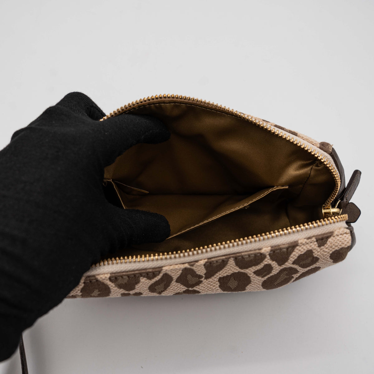 Coach cosmetic pouch in brown and beige leopard print canvas with chocolate leather trim and gold hardware, shown with wrist strap.