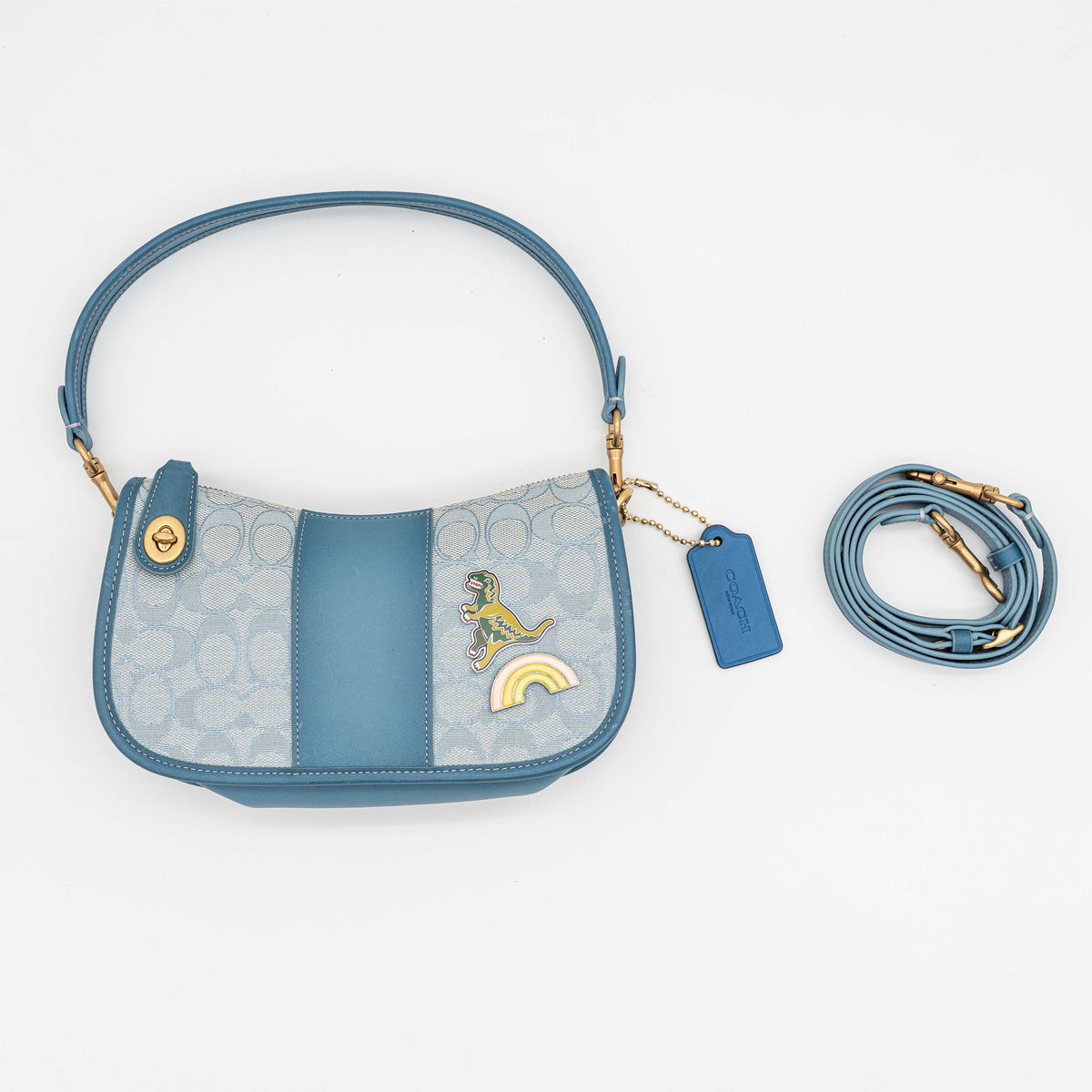 Coach 2Way Signature Swinger Shoulder Bag in light blue monogram canvas and leather with dinosaur and rainbow patches, shown with detachable strap.