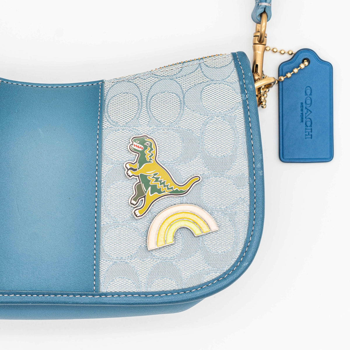 Coach 2Way Signature Swinger Shoulder Bag in light blue monogram canvas and leather with dinosaur and rainbow patches, shown with detachable strap.