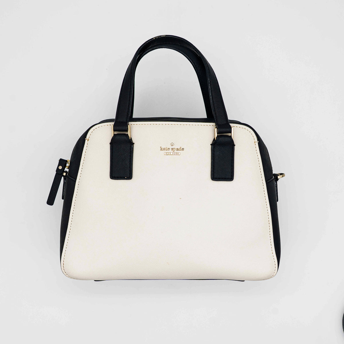 Kate Spade Cameron Street Little Babe satchel in black and white leather with gold hardware, shown with dual handles against a minimal background.