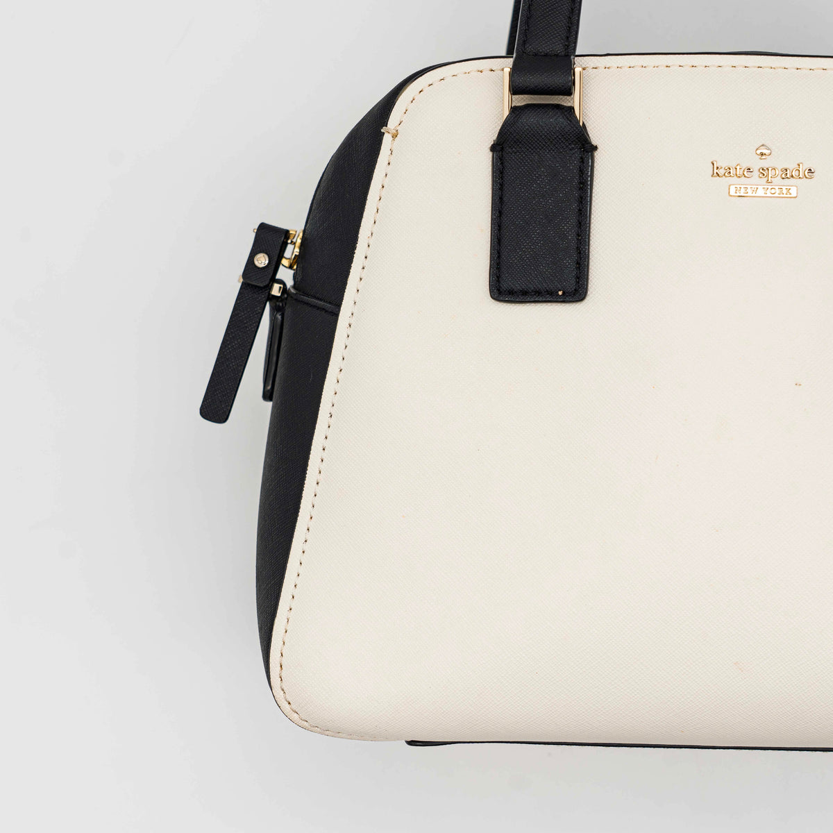 Kate Spade Cameron Street Little Babe satchel in black and white leather with gold hardware, shown with dual handles against a minimal background.